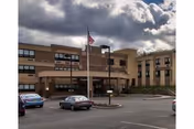 Front view of Achieve Rehab and Nursing Facility building with American flag and parking.