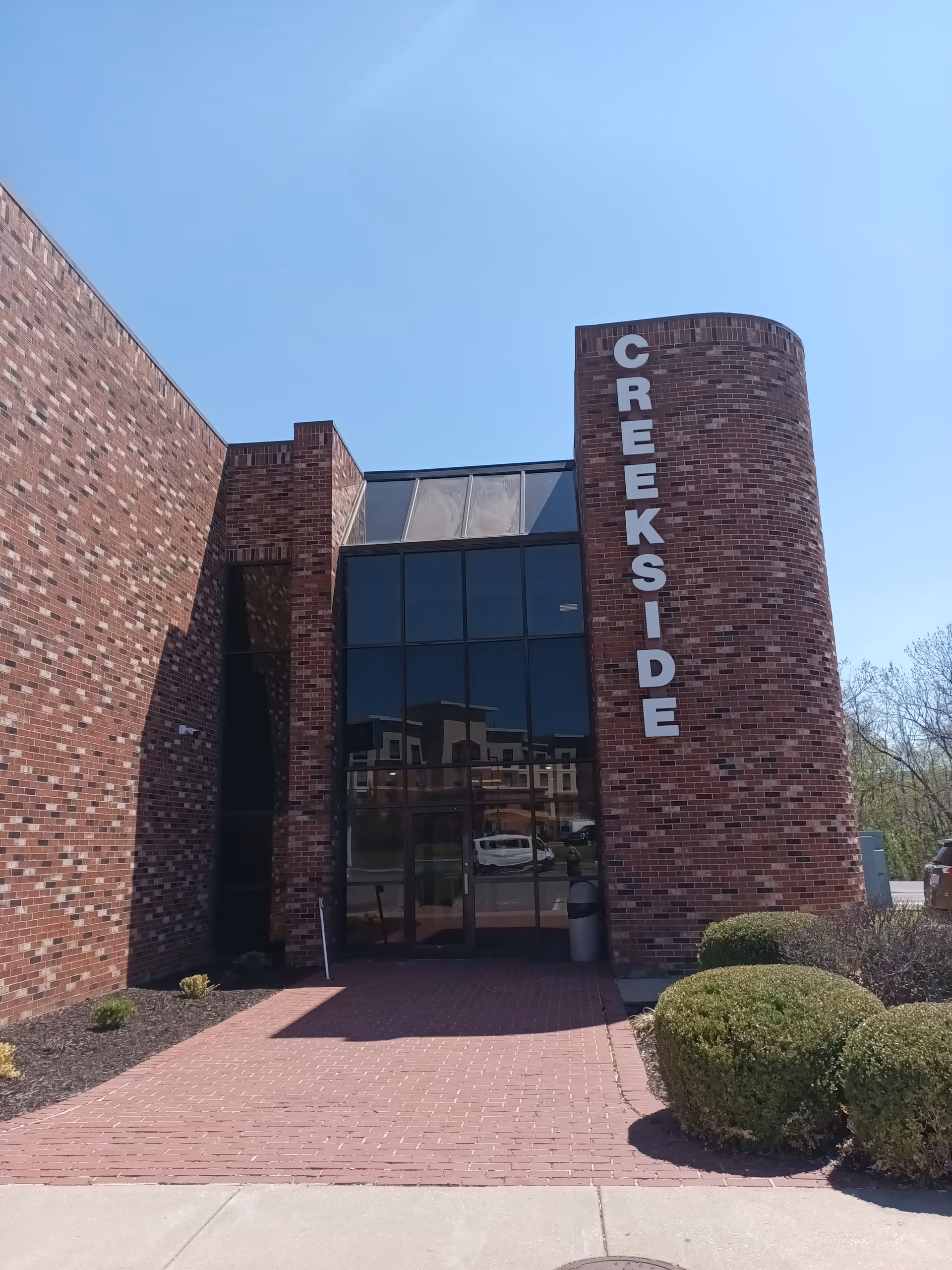 Brick building exterior with Creekside sign and glass entrance on a sunny day.