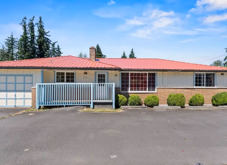 Single-story facility with red roof, blue ramp railing, brick façade, and trimmed shrubs.