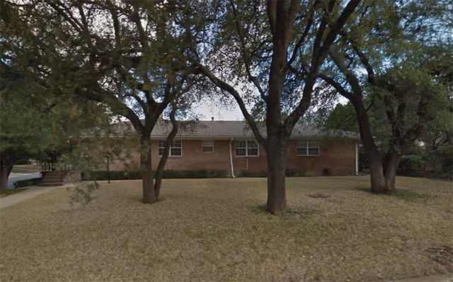 Brick facility building with windows, surrounded by trees and a grassy lawn.