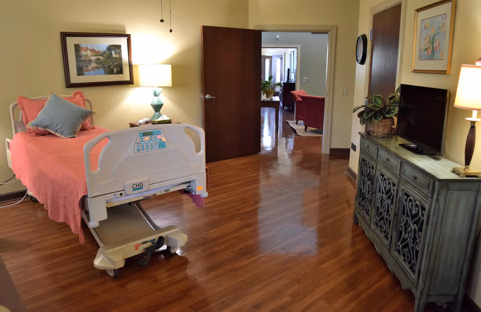 Hospice room with a pink hospital bed, dresser, and wooden floors.