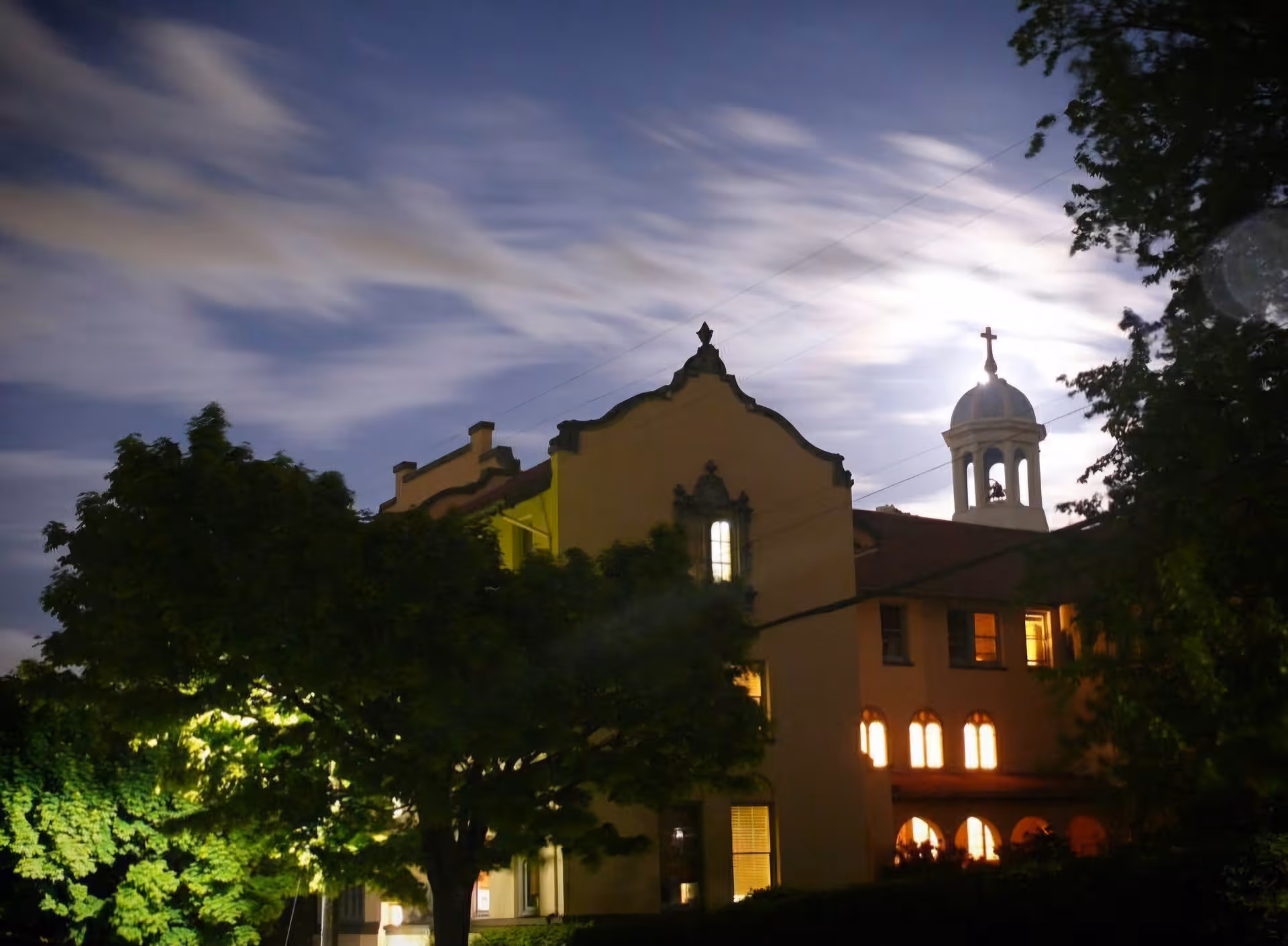 Night exterior of a church-like memory care facility with illuminated windows and trees
