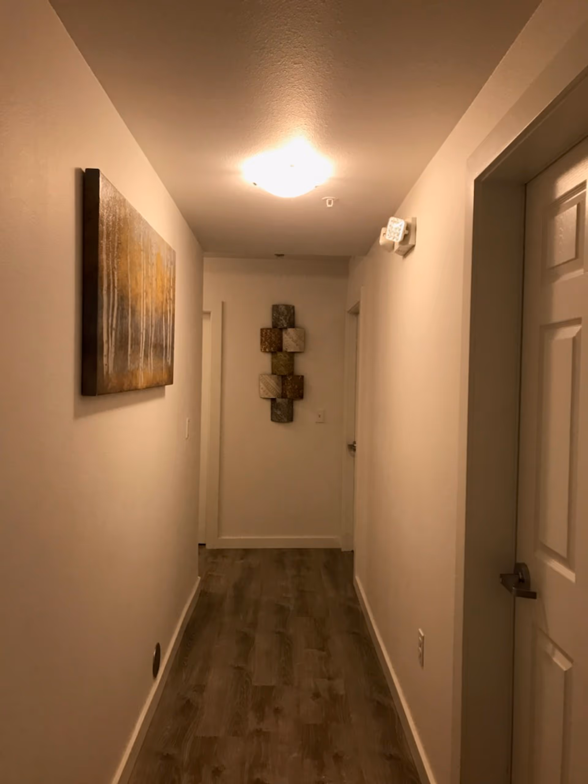 Narrow interior hallway in a senior living facility, with wall art and a ceiling light.