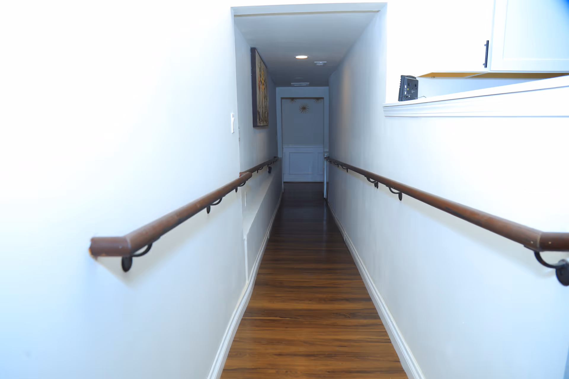 Long corridor in a senior living facility with handrails and a door at the end.