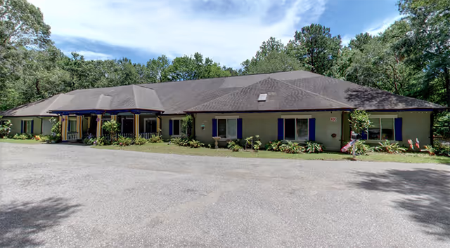 Single-story building with blue shutters and landscaped front, surrounded by trees.