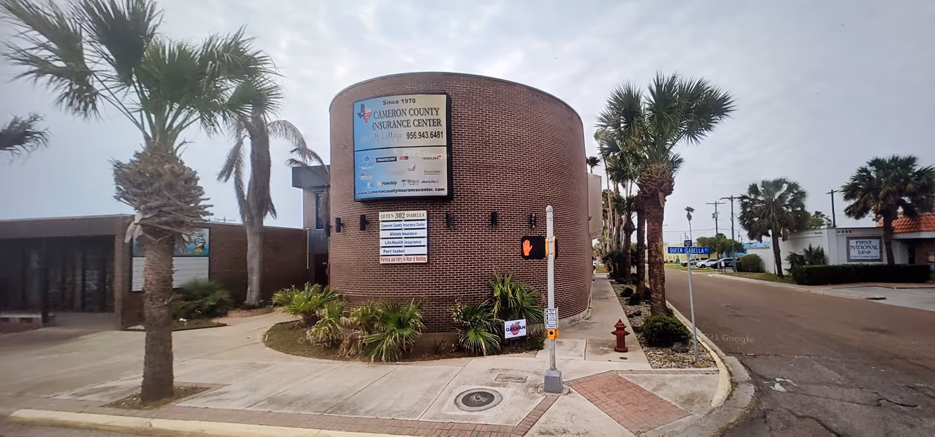 Brick curved front building with signs, palm trees, and a sidewalk at a street corner.