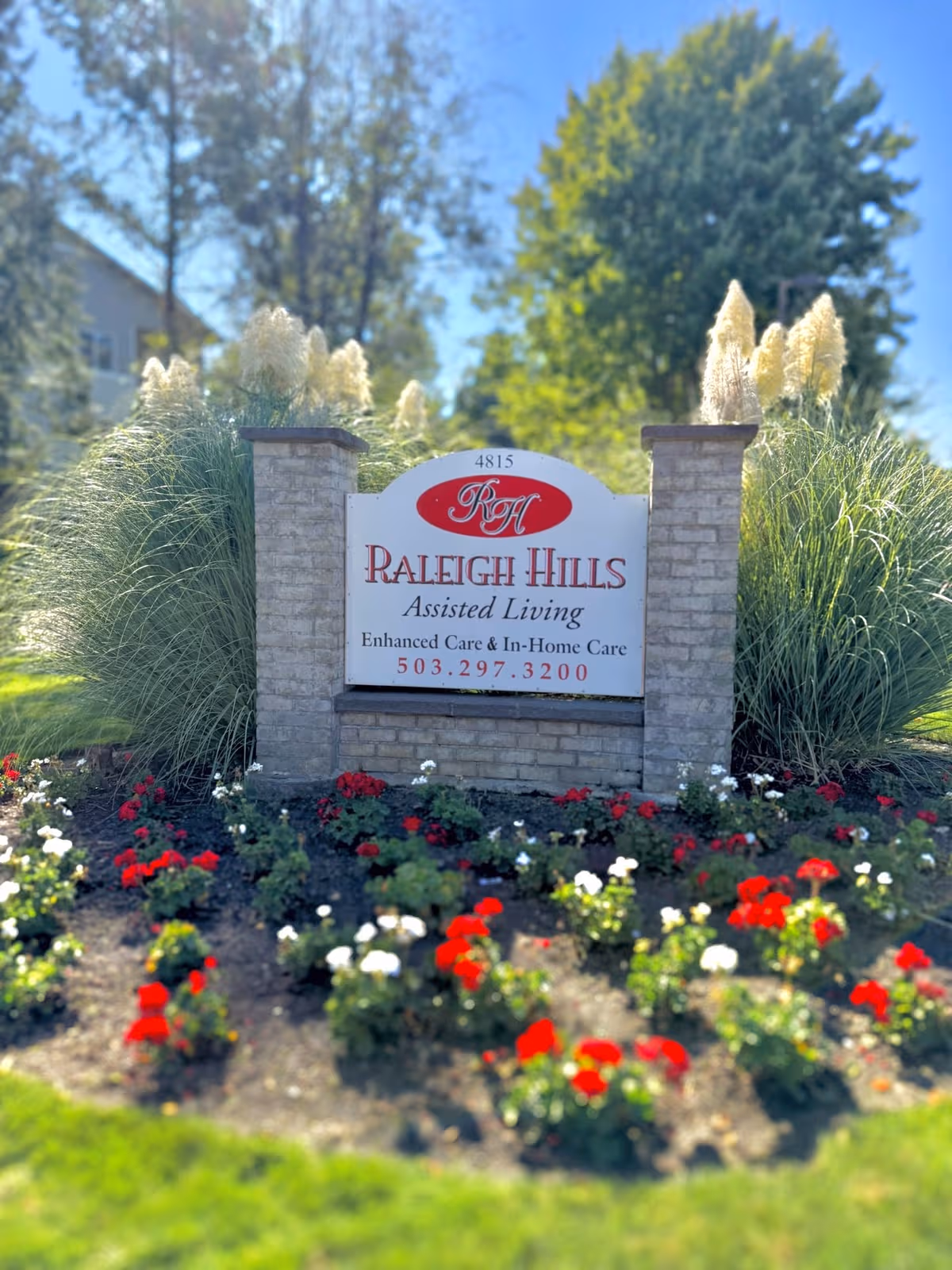Entrance sign for Raleigh Hills Assisted Living surrounded by blooming flowers and landscaping.