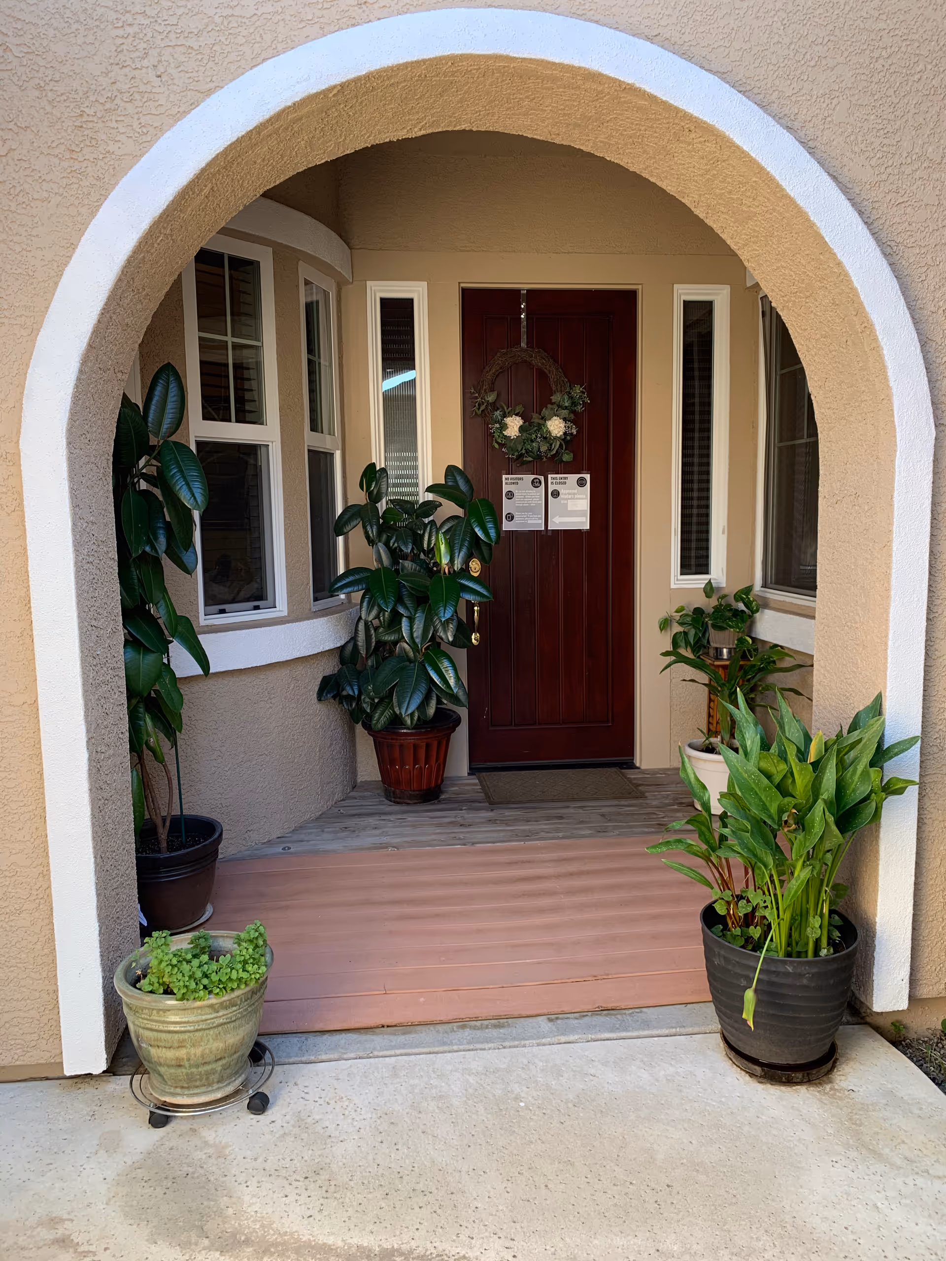 Arched entryway of Tender Home Senior Care with potted plants and wreath on a red door.