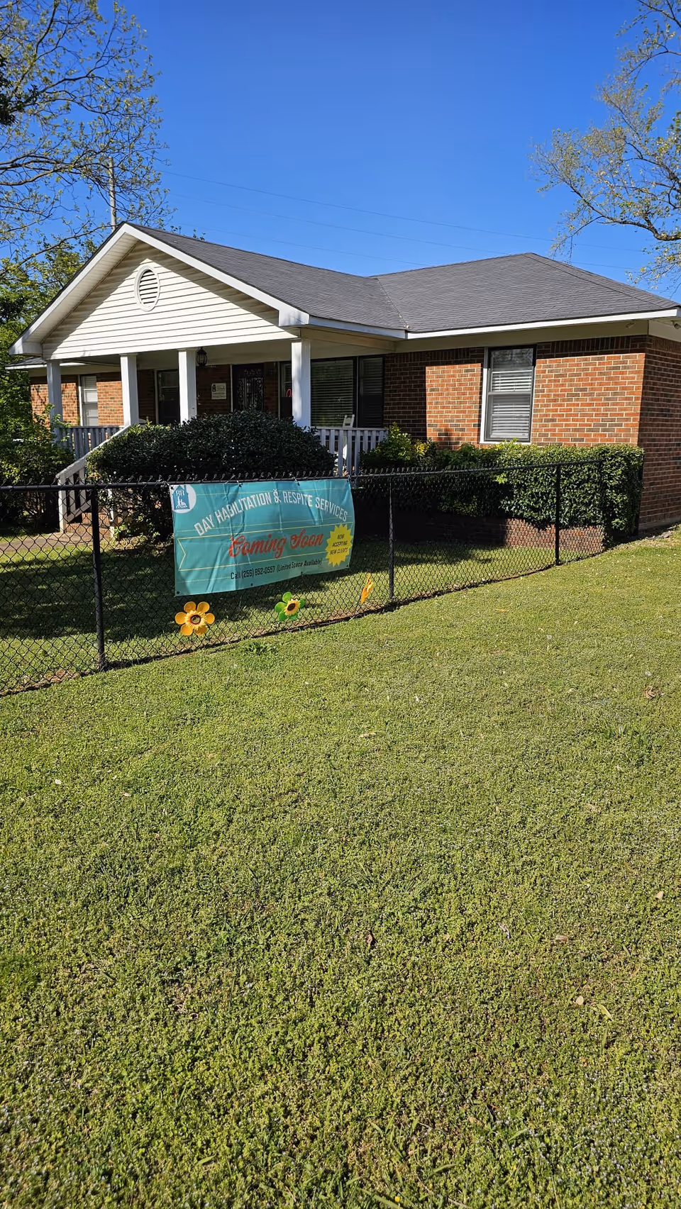 Front exterior of a brick facility with a porch and a banner on a chain-link fence.