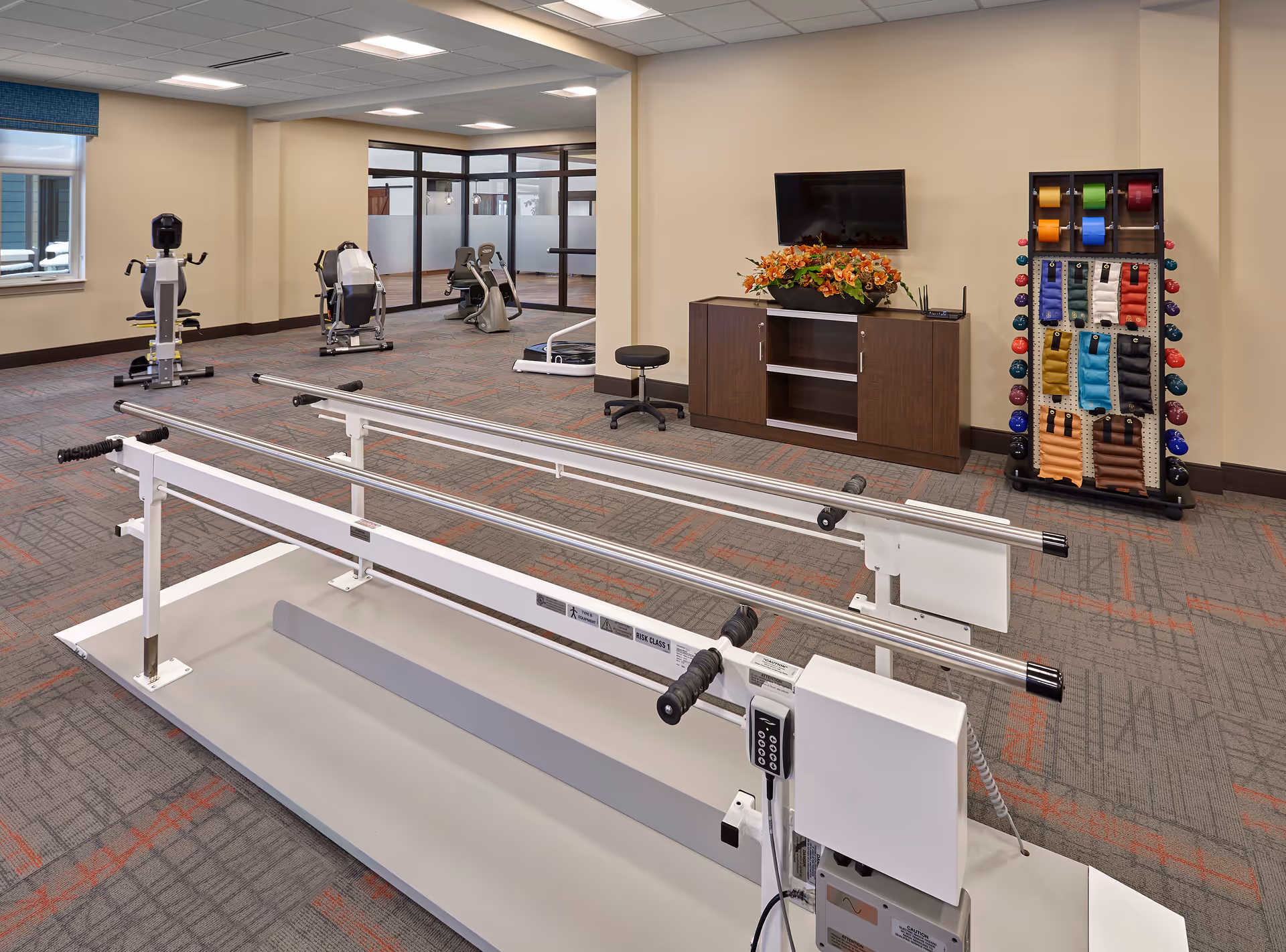 Bright interior fitness room with parallel bars, cardio machines, and a towel display.