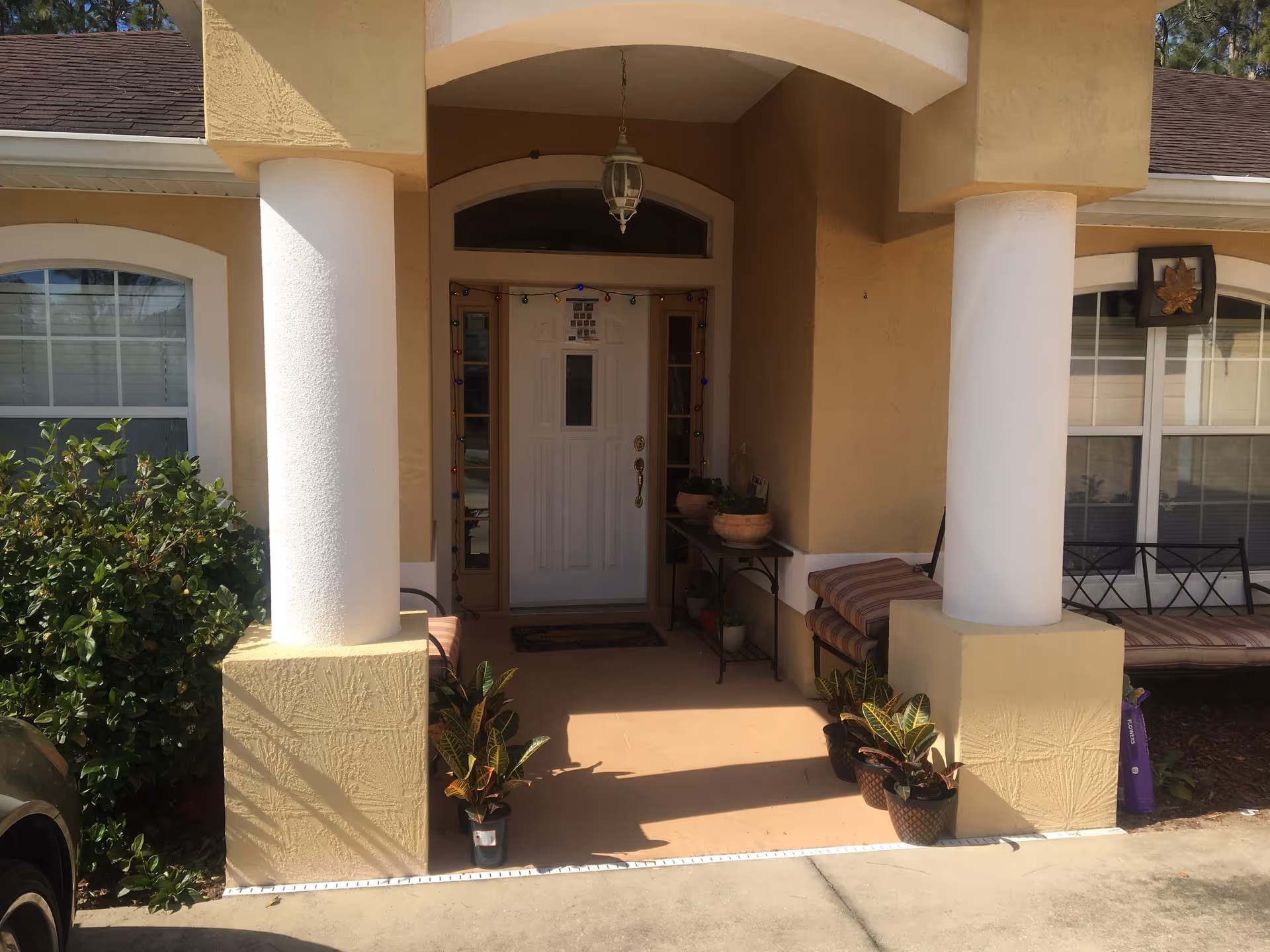 Front entrance of Gihon Family Care Home, a beige facility with columns, porch seating, potted plants.