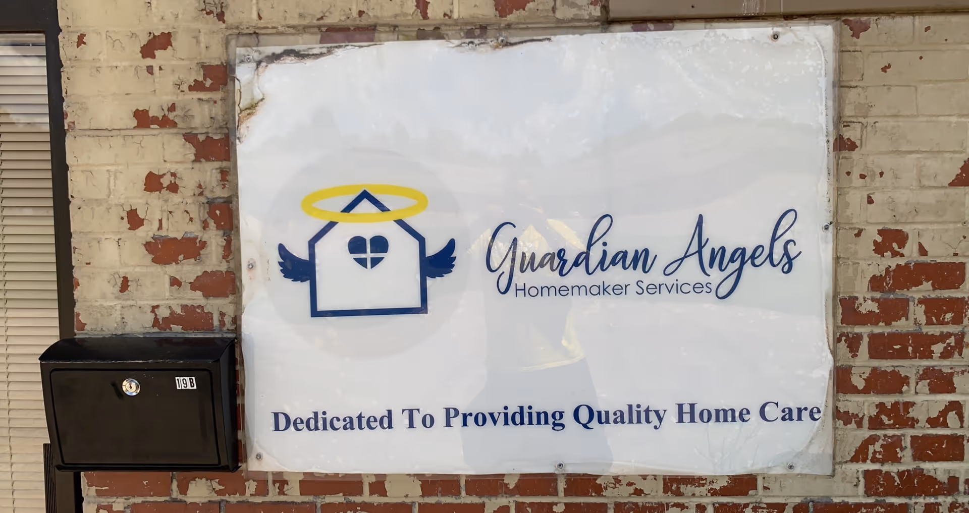 Exterior brick wall with Guardian Angels Homemaker Services sign and a black mailbox.