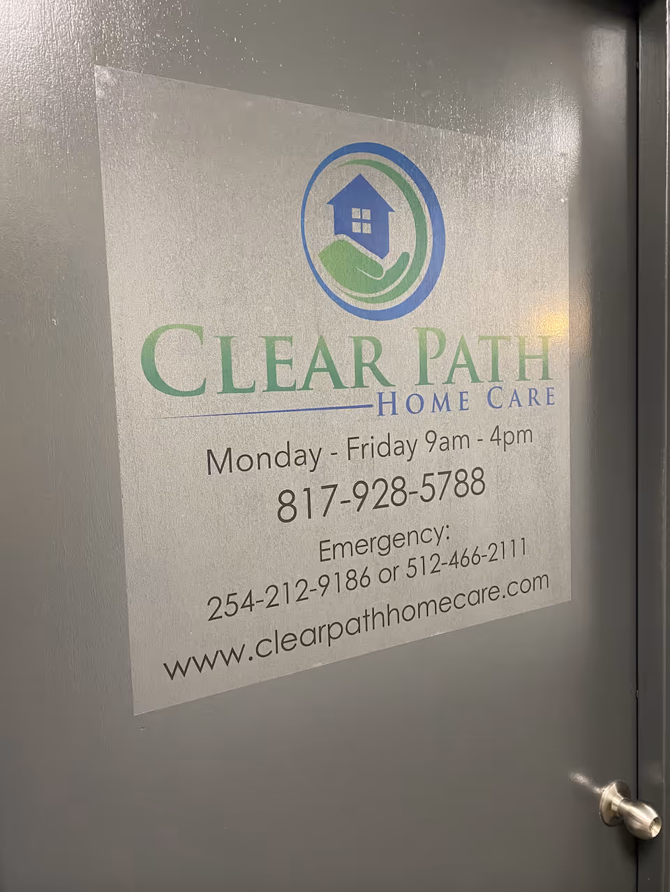Sign on a gray door advertising Clear Path Home Care with hours and contact info.