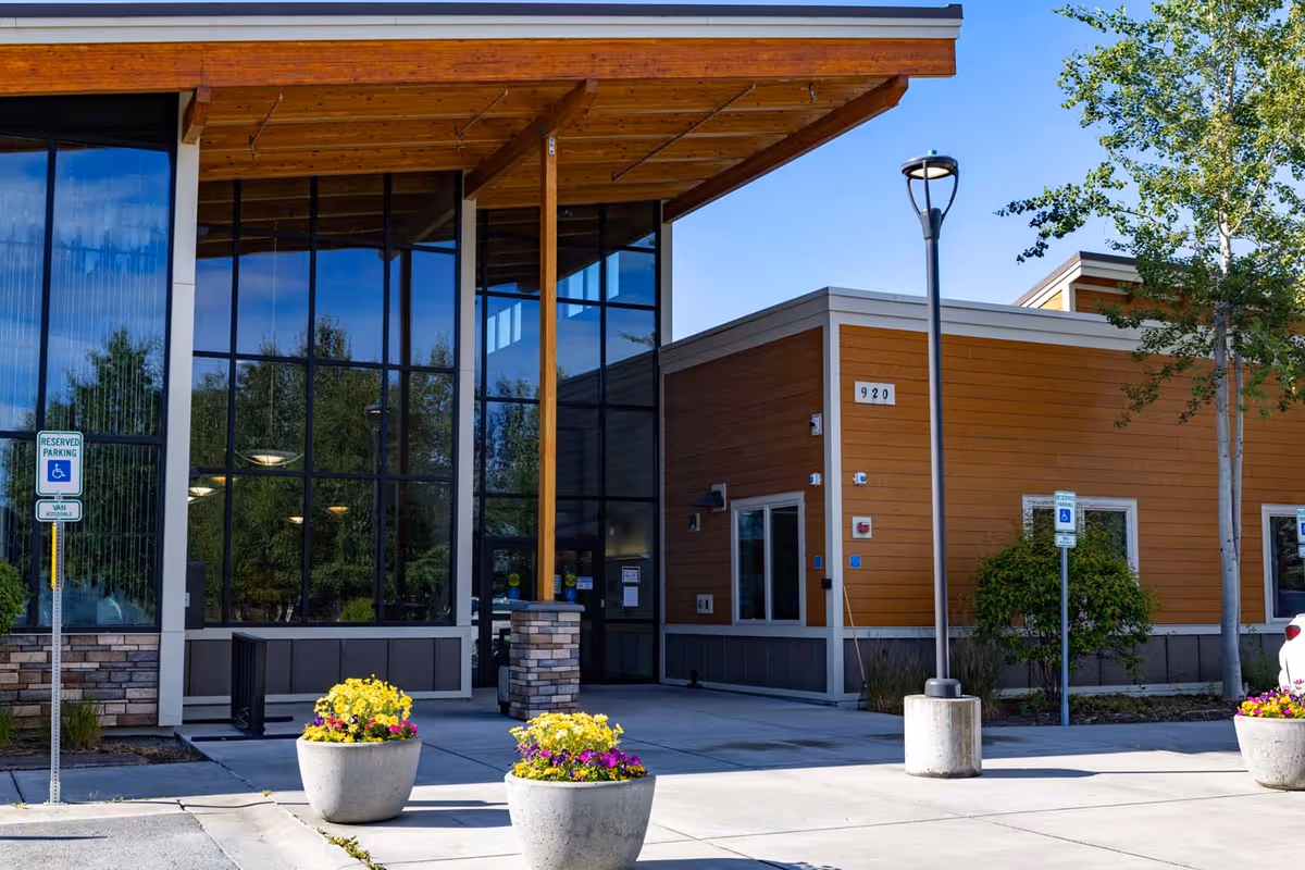 Modern senior living facility exterior with timber accents, large glass façade, and flowering planters.