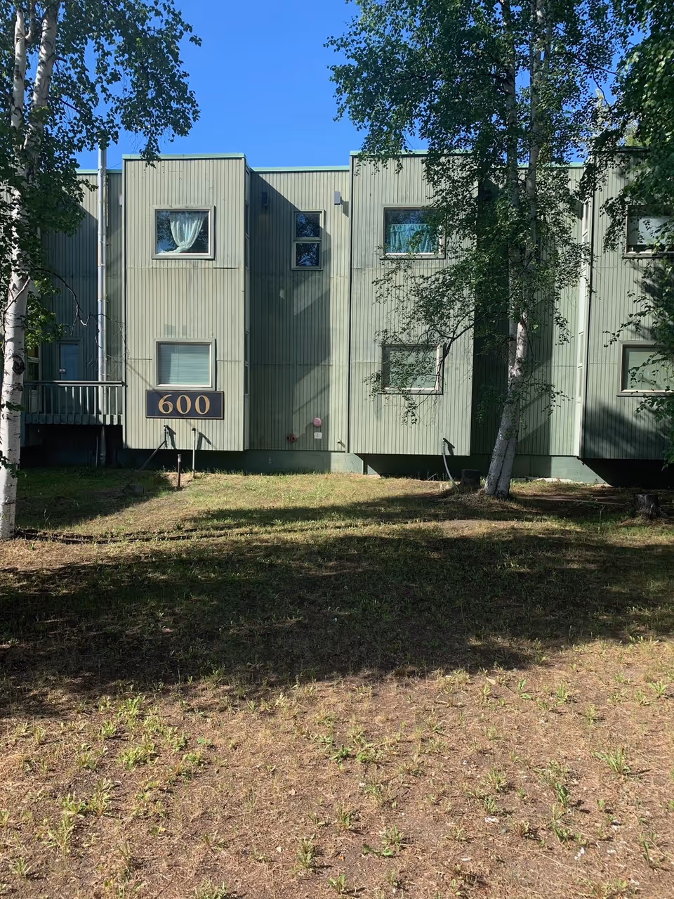 Front view of a green multi-unit senior living building with trees and grass.