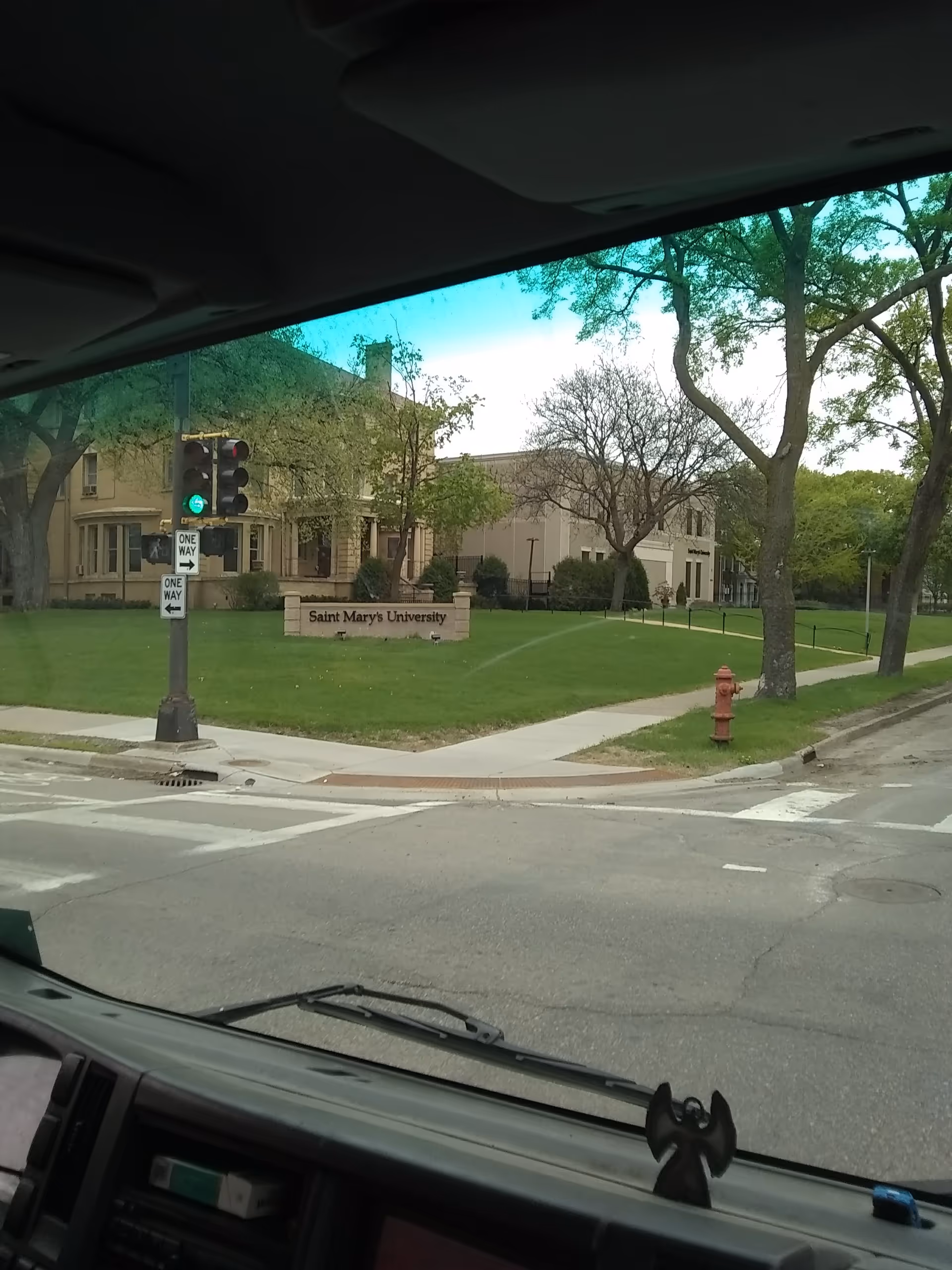 From inside a car, a street scene shows a university building and green lawn.