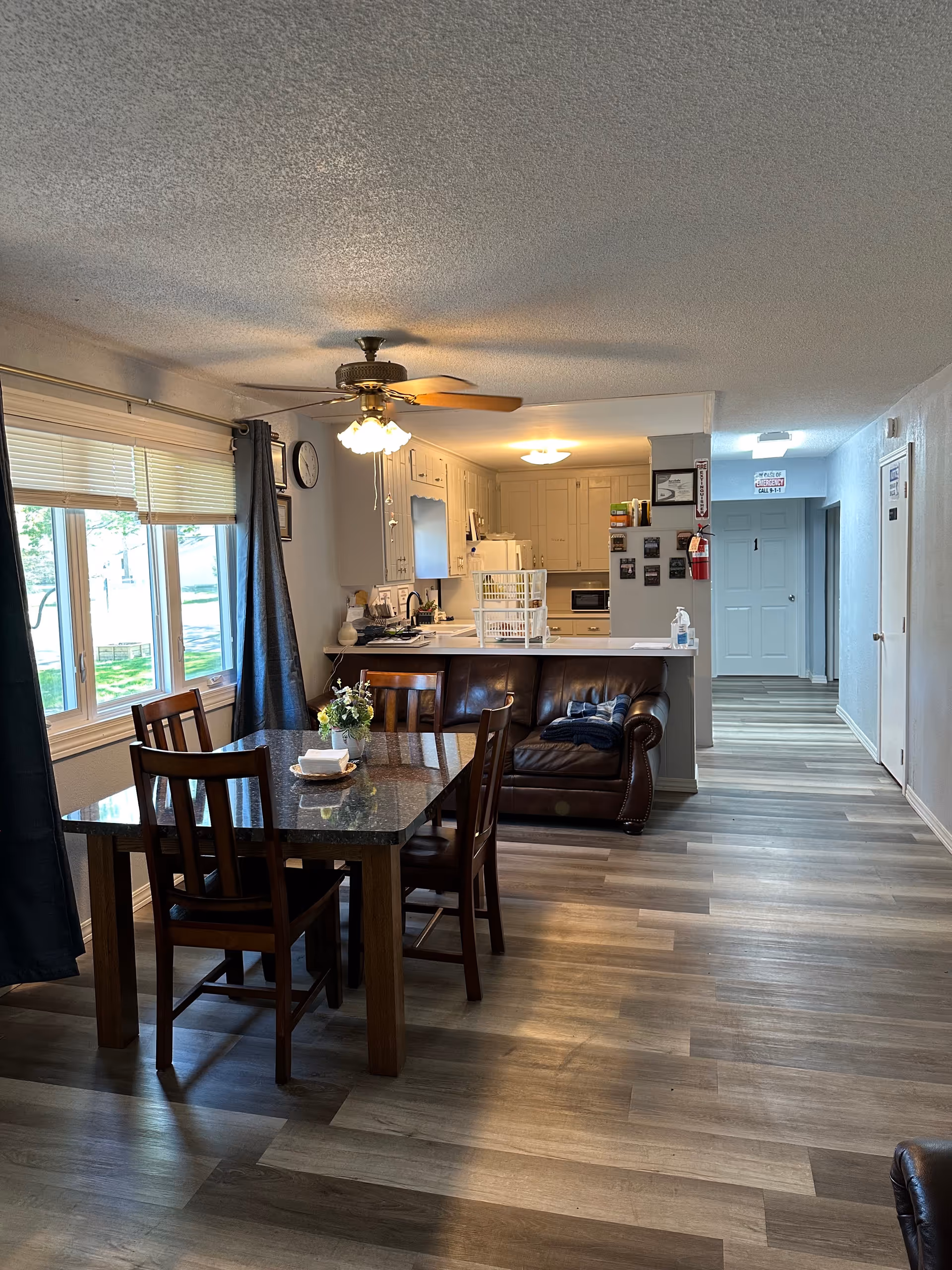 Open dining area with a wooden table, chairs, and a brown leather sofa near the kitchen.