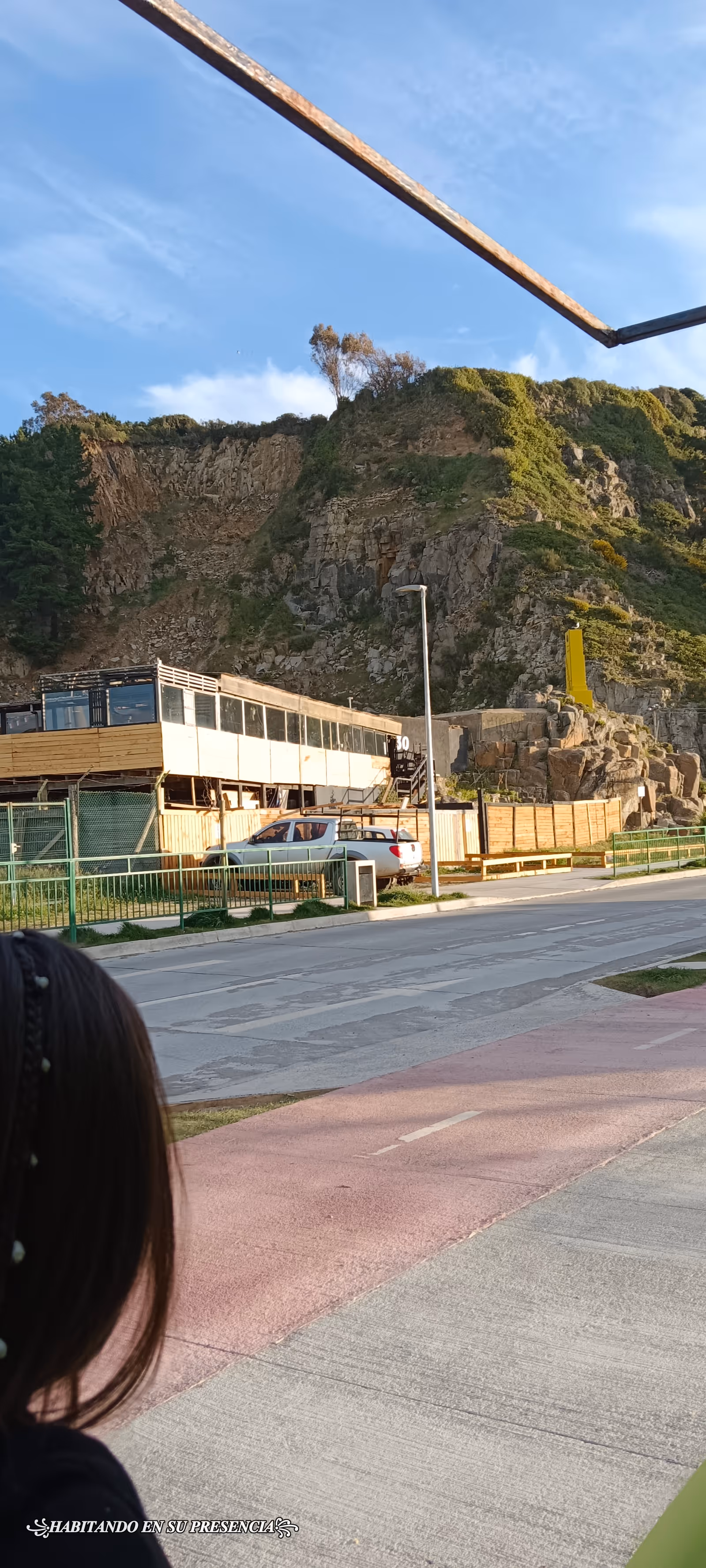 Outdoor hillside scene with a modern exterior building, railing, parked car, and road.