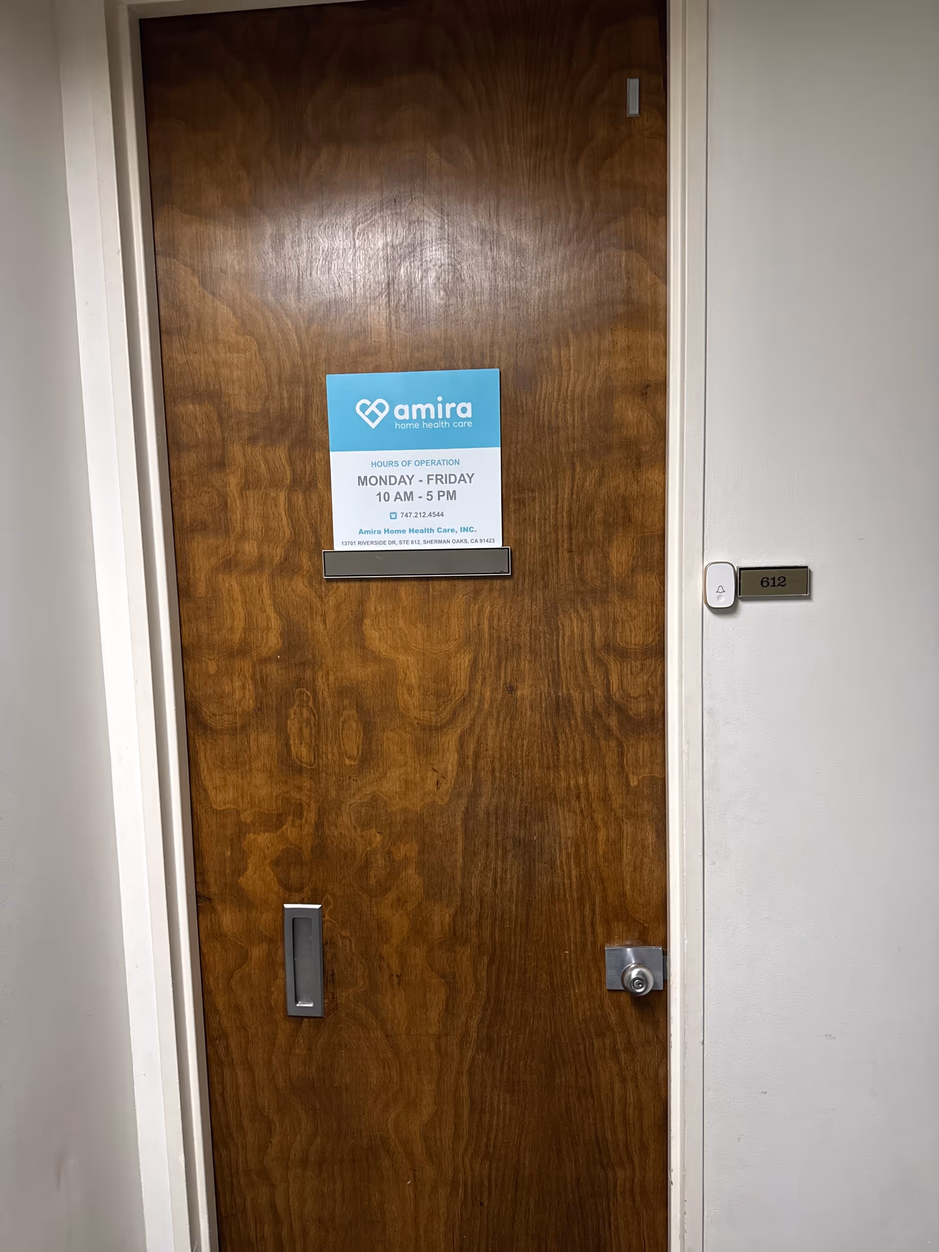 Wooden interior door with an Amira Home Health Care sign posted in a hallway.