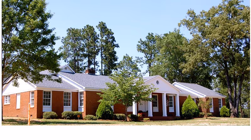 Brick senior living facility with white columns and surrounding trees.