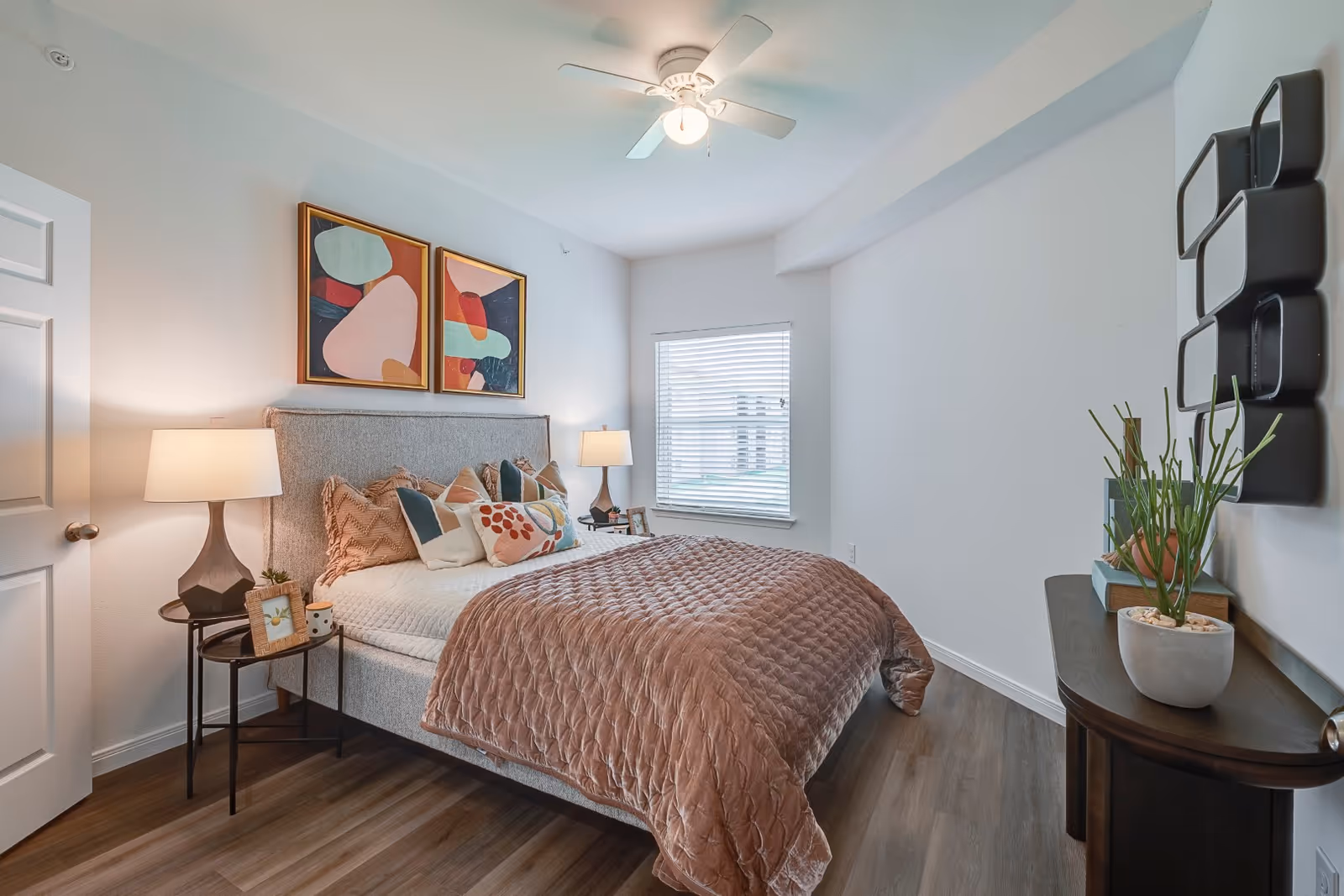 Bright bedroom in a senior living facility featuring a cozy bed, nightstands, lamps, and art.