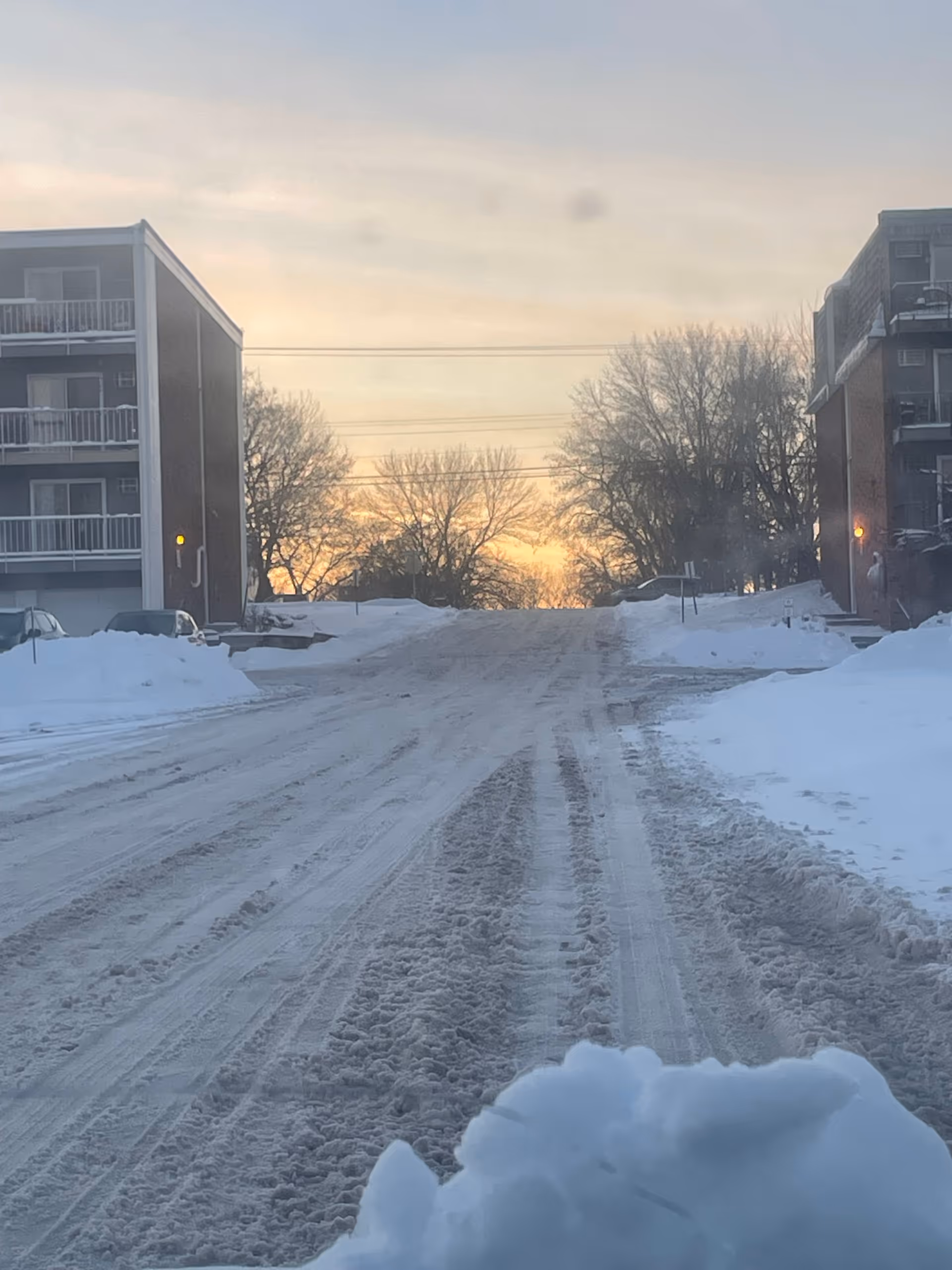 Snowy street between apartment buildings at sunset.
