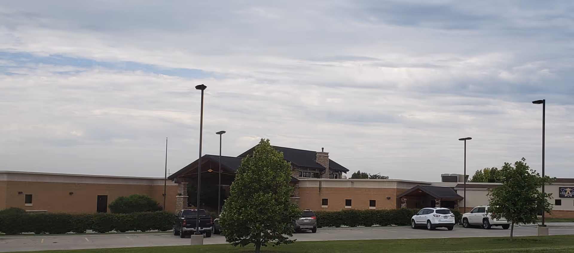 Exterior view of a low-rise hospital building with a parking lot and trees.