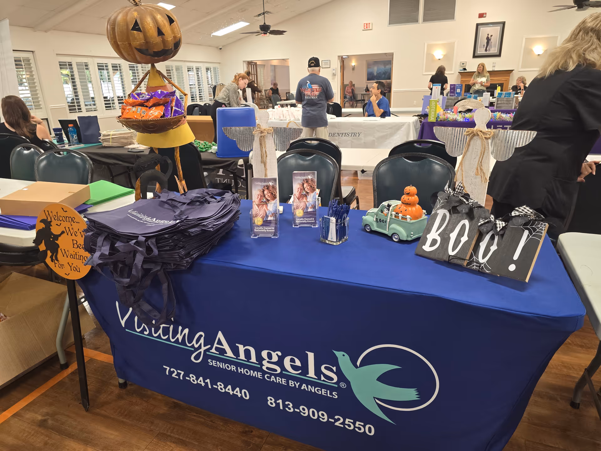 Indoor care fair featuring a blue Visiting Angels table and staff members