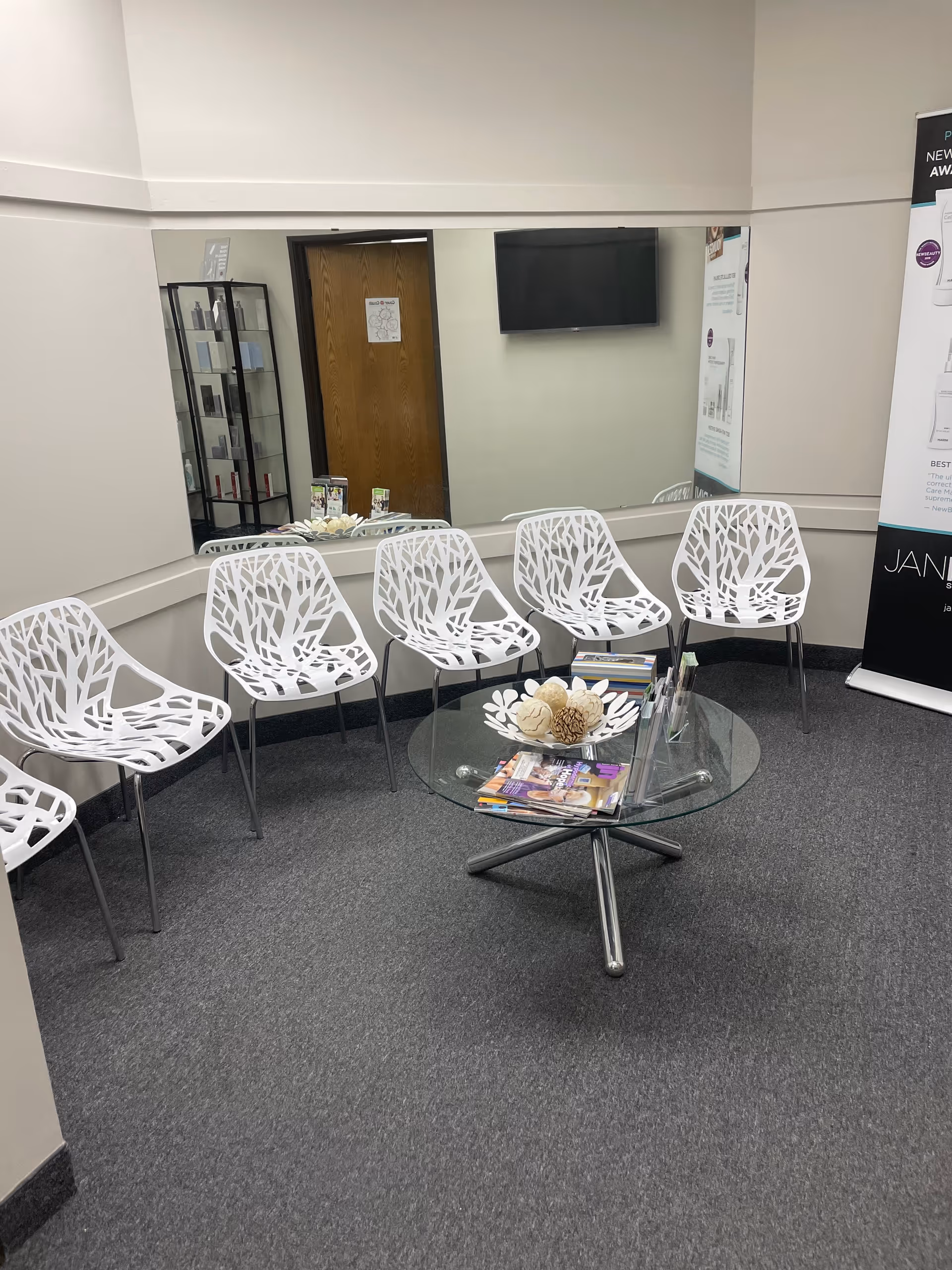 Minimalist waiting area with white tree-pattern chairs around a glass coffee table and magazines.