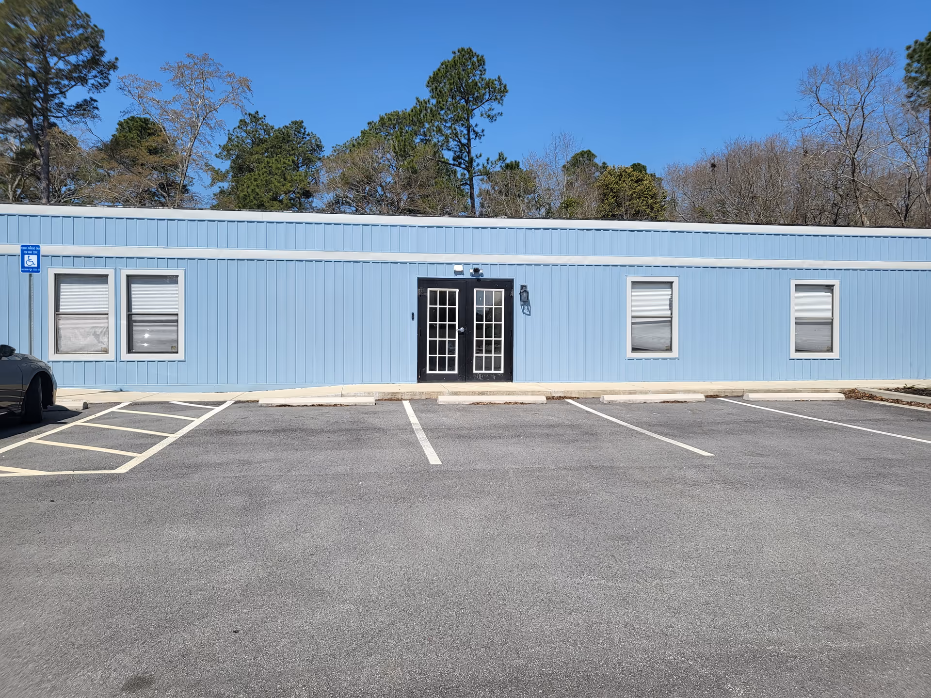 Blue, single-story facility exterior with a parking lot and surrounding trees.