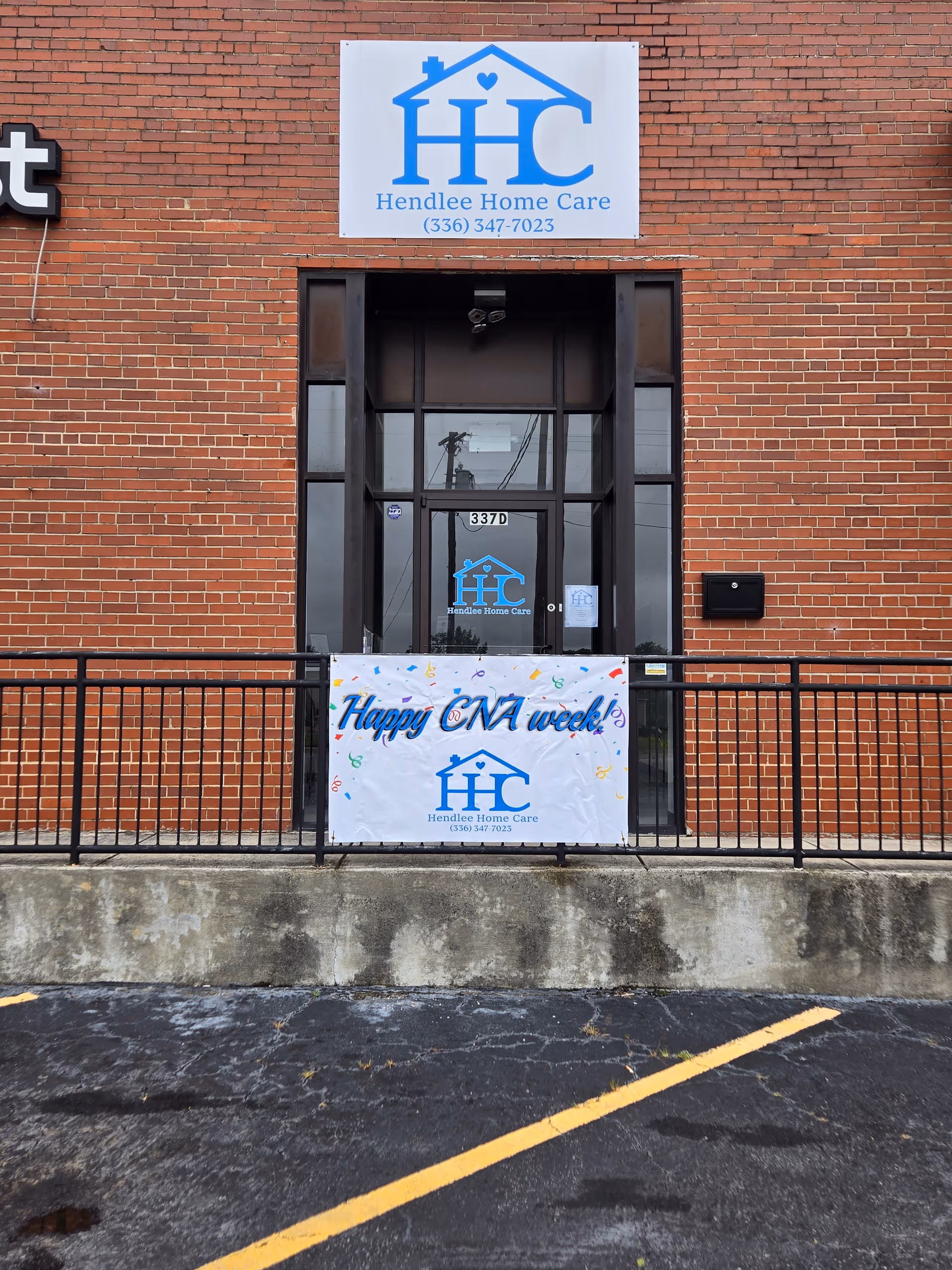 Brick building entrance with Hendlee Home Care sign and festive CNA week banner.