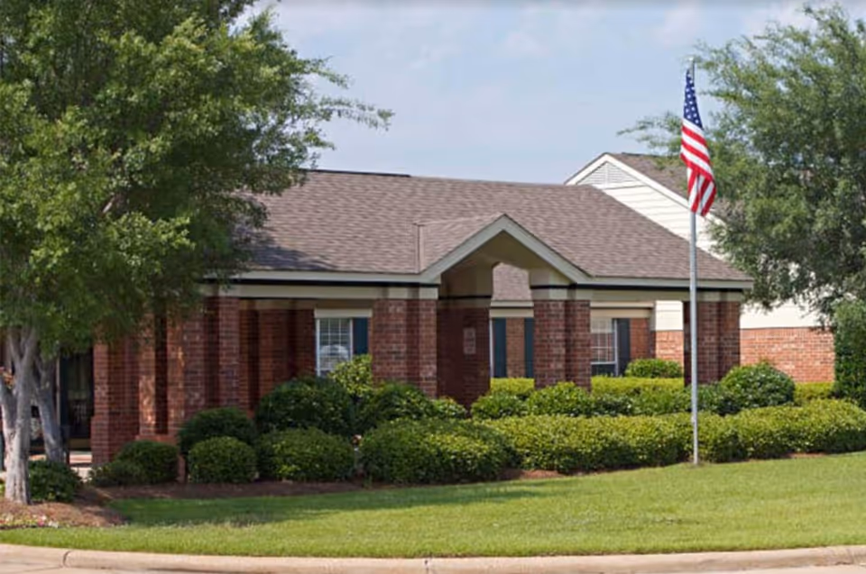 Brick senior living facility entrance with manicured shrubs and American flag