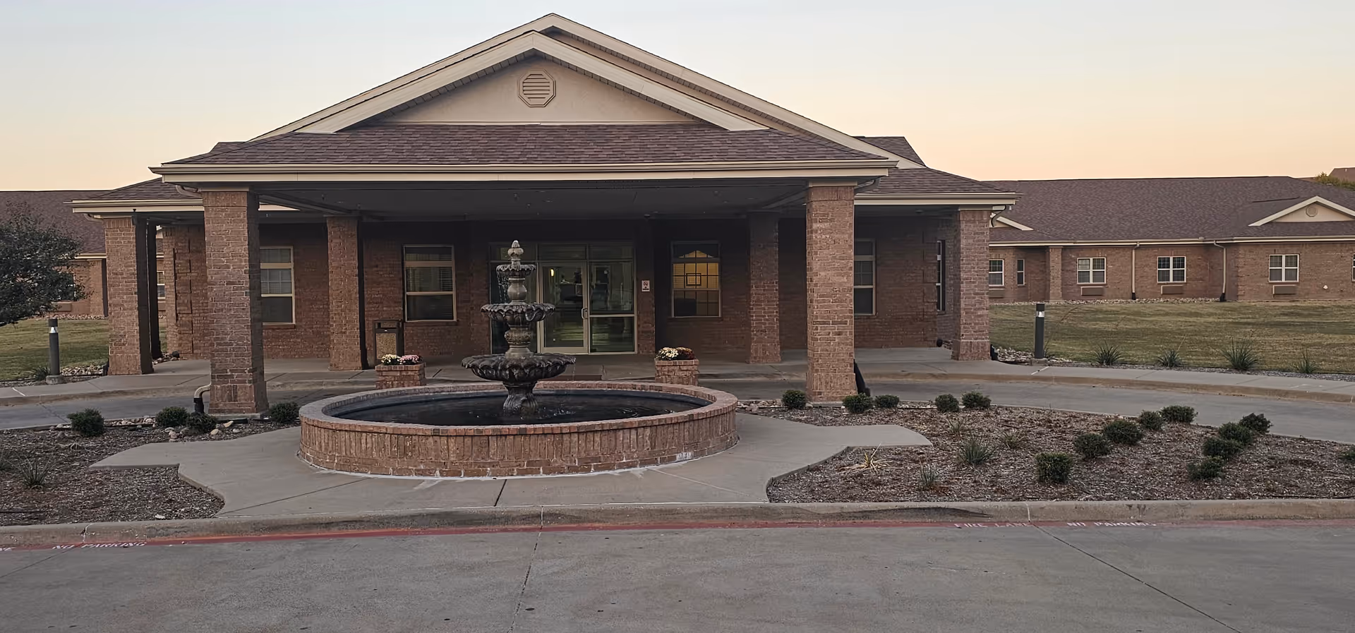 Brick senior living facility exterior with a circular fountain and covered entrance.