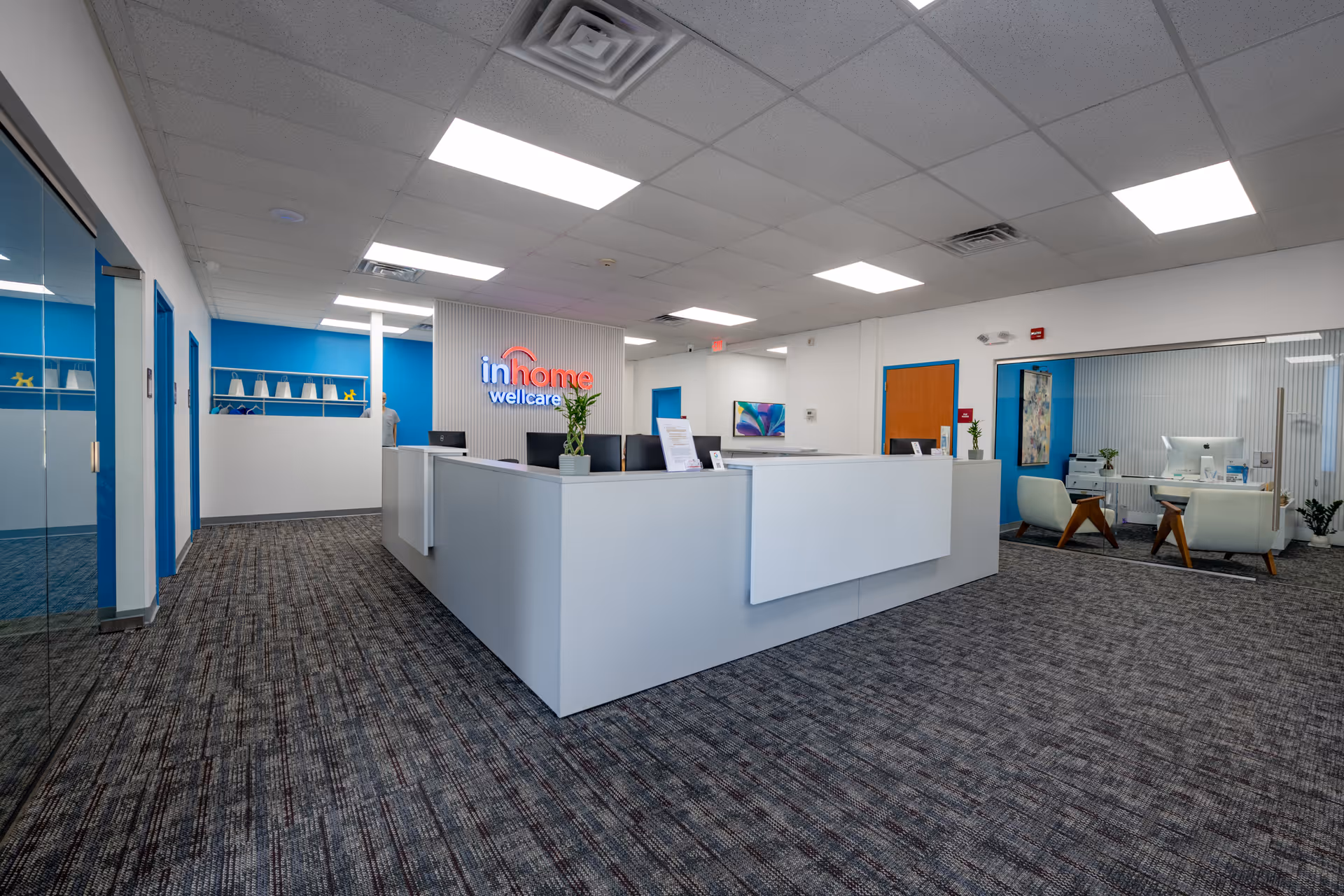 Reception area with white desk, bright lighting, and In Home Wellcare sign.