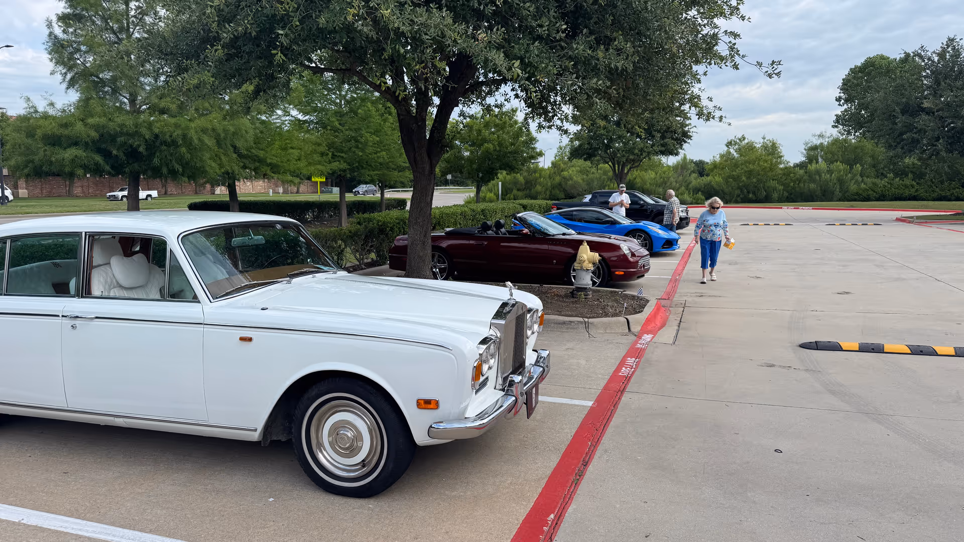 Classic white car in a parking lot at a senior living campus with people nearby