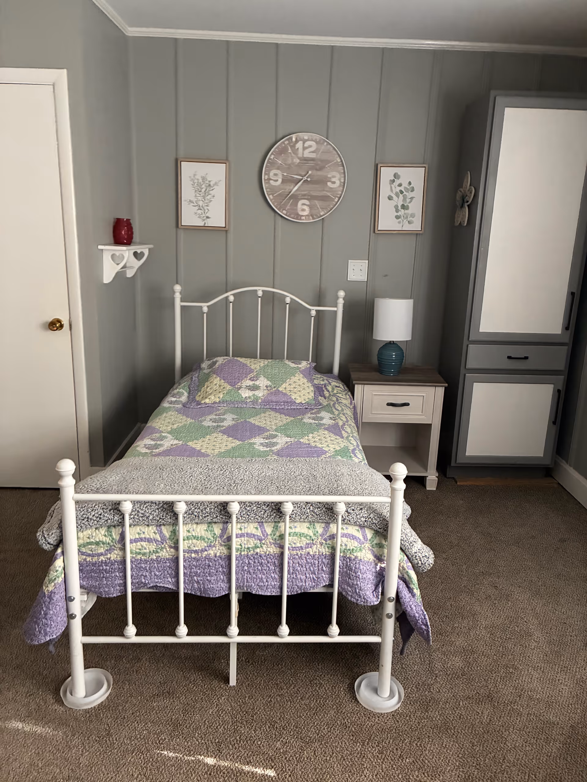 Cozy bedroom with a white metal bed, quilt, nightstand, and a wardrobe.