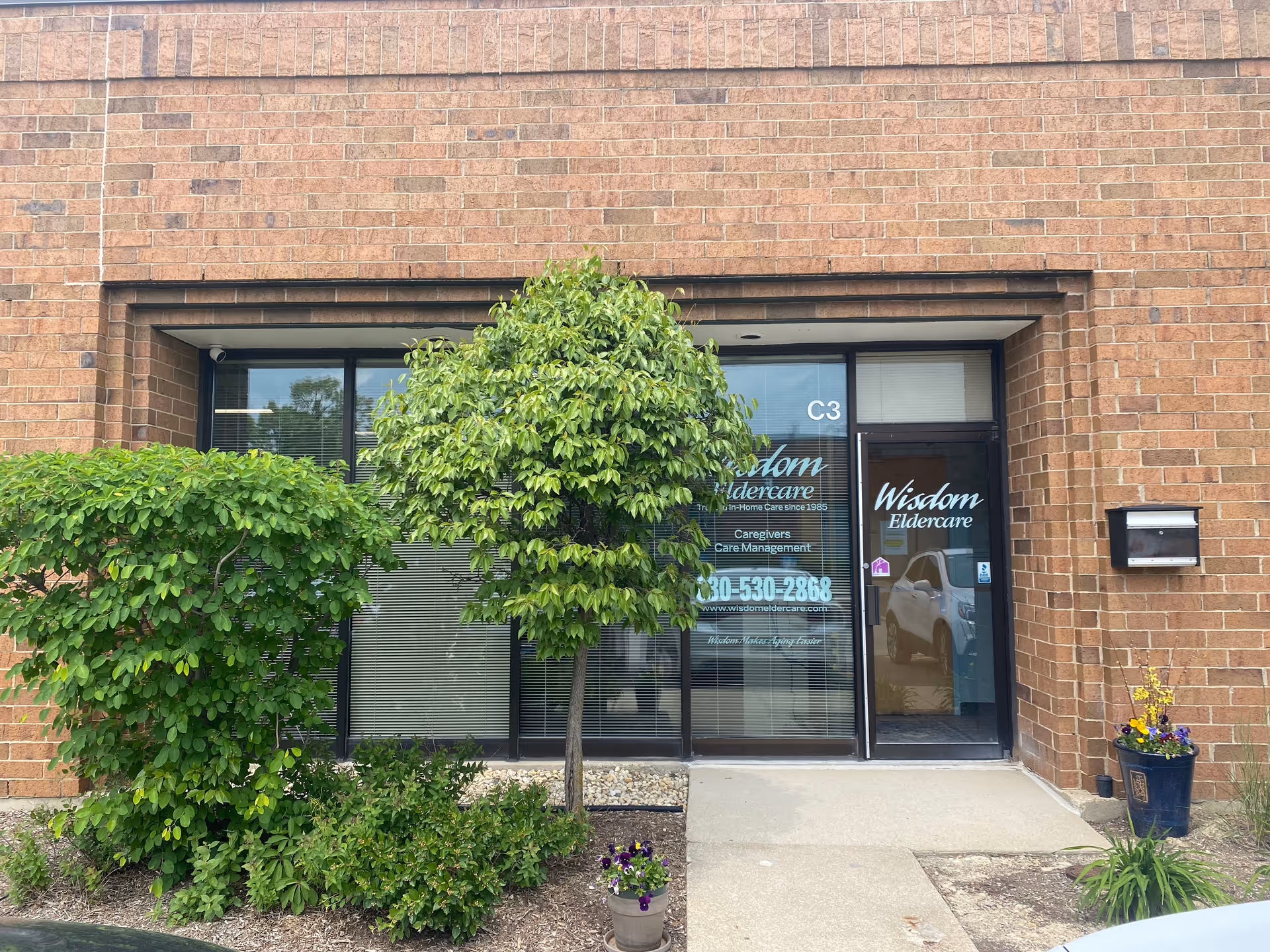 Brick storefront entrance for Wisdom Eldercare with glass doors and surrounding greenery.