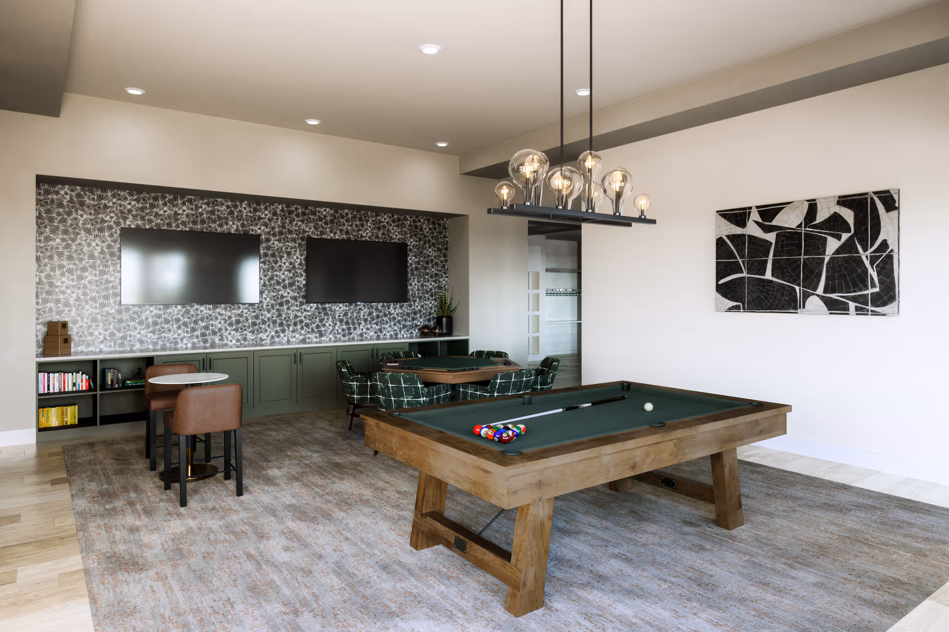 A spacious community recreation room featuring a wooden pool table, seating, TVs, and decorative lighting.