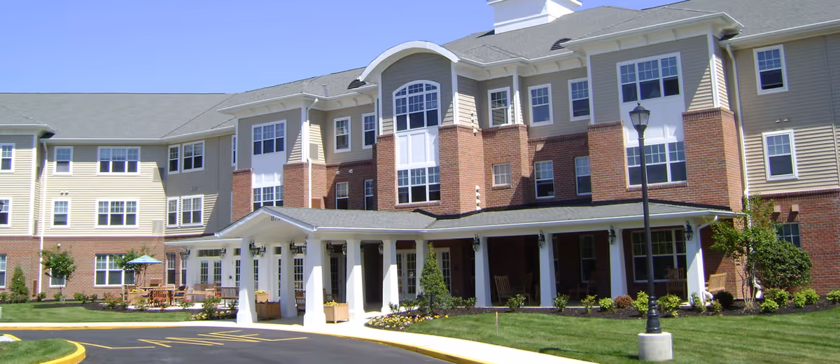 Two story senior living building with beige siding, brick accents, and a welcoming entrance canopy.