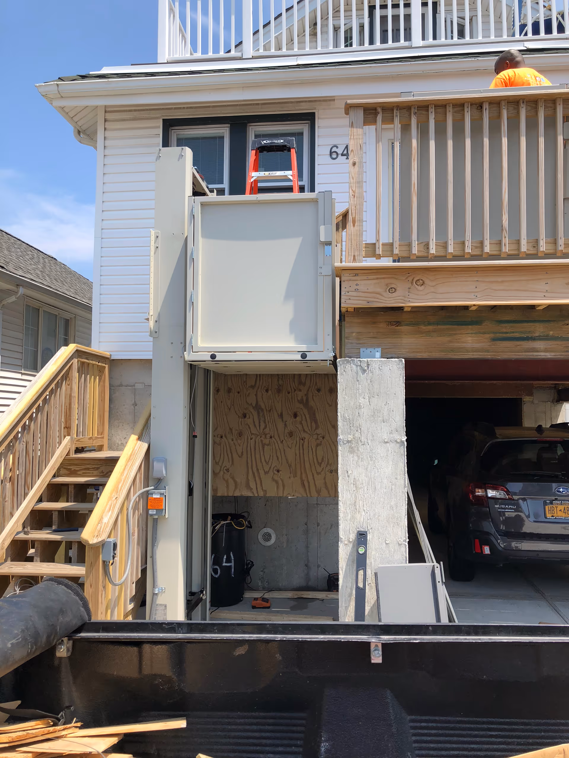Two-story house exterior under renovation with stairs, balcony, and construction equipment