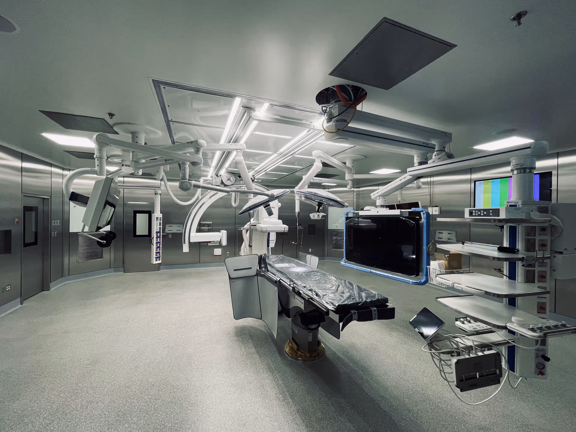 Sterile operating room with advanced surgical equipment, overhead arms, monitors, and a central patient table.