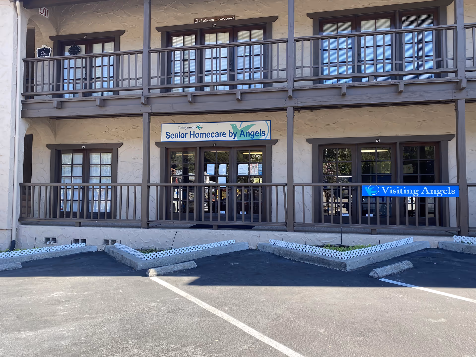 Two-story, wood-framed building with balconies and signs for Senior Homecare by Angels and Visiting Angels.