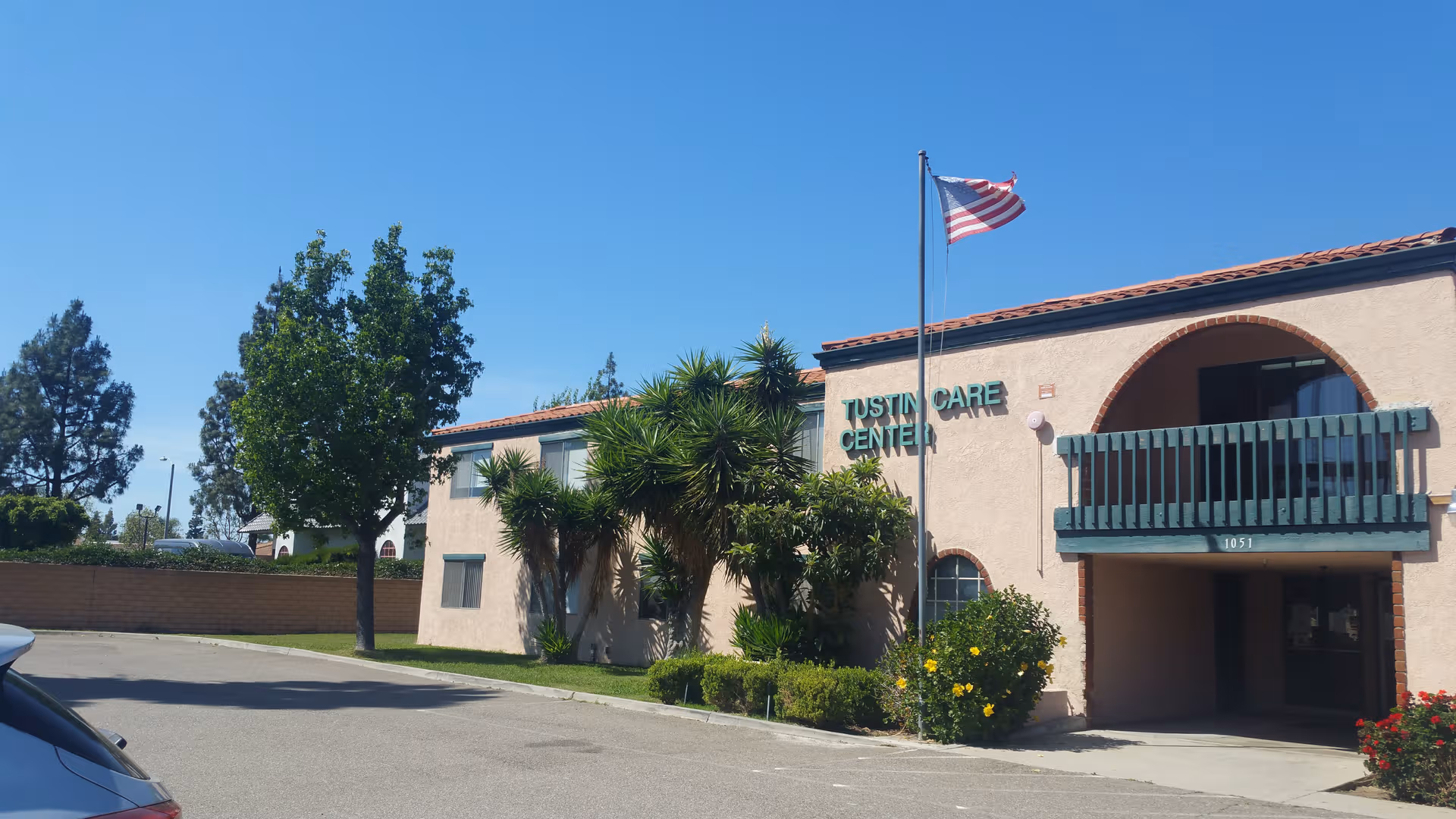 Exterior view of Tustin Care Center with entrance, greenery, and an American flag.