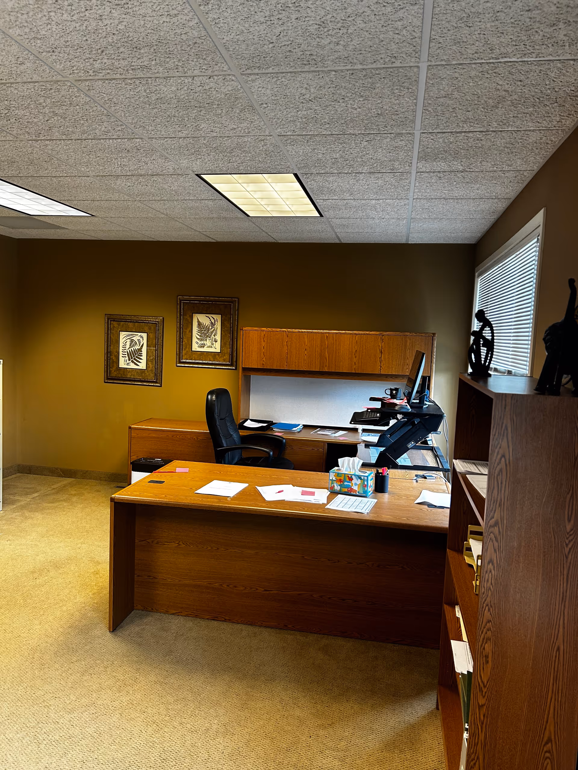 Wooden desk with computer and chair in an office setting with brown walls.