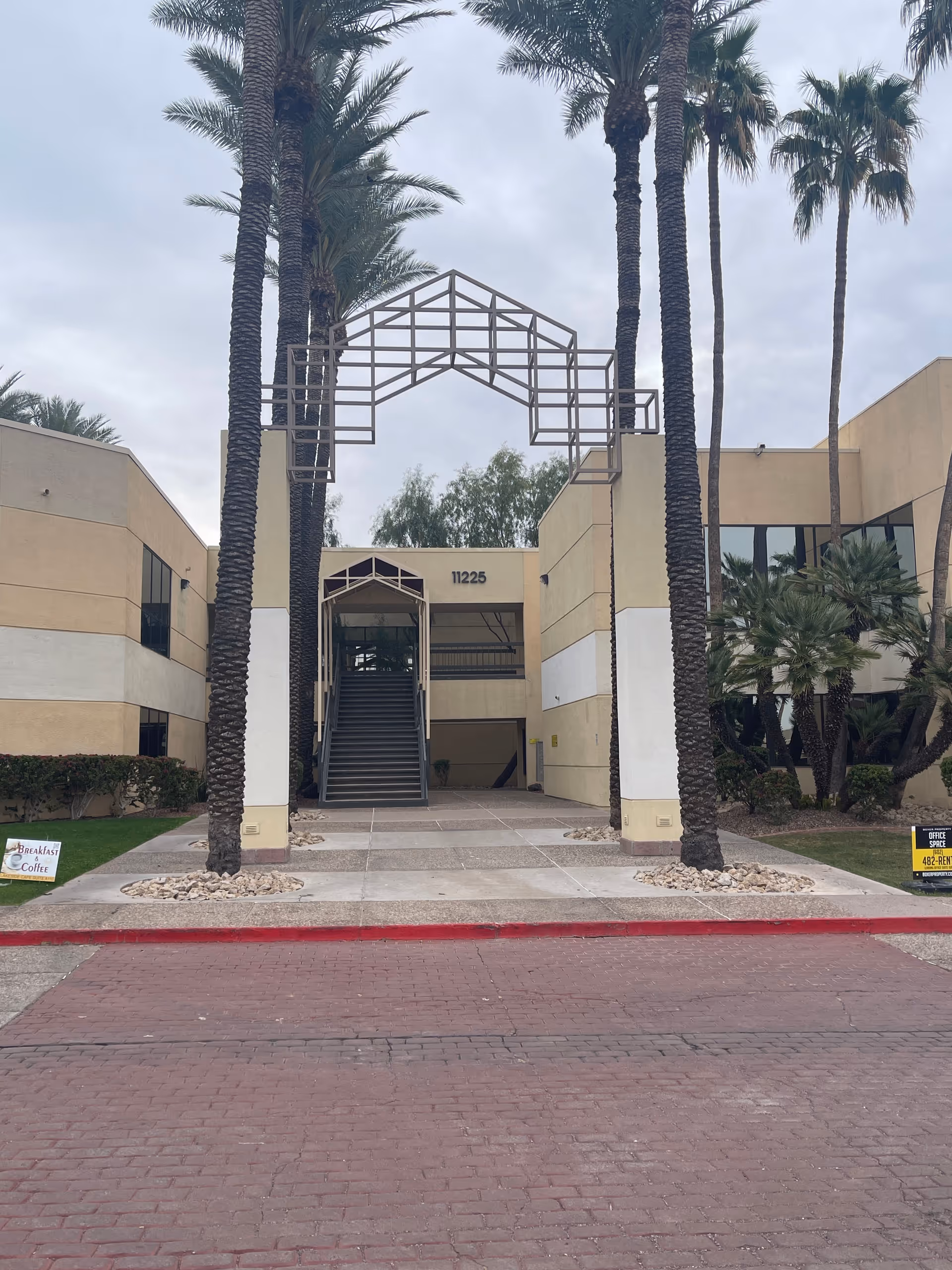 Front exterior of a beige building with palm trees, steps, and a metal archway.