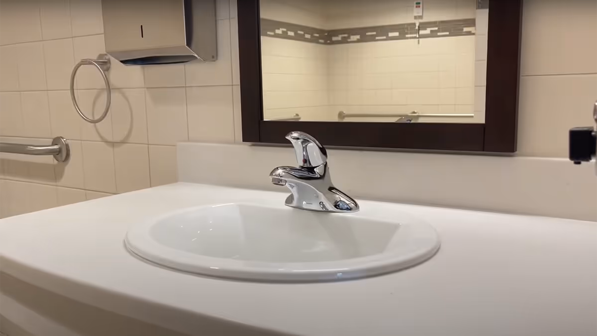 Sleek bathroom sink with chrome faucet and framed mirror in tiled, accessible facility restroom.