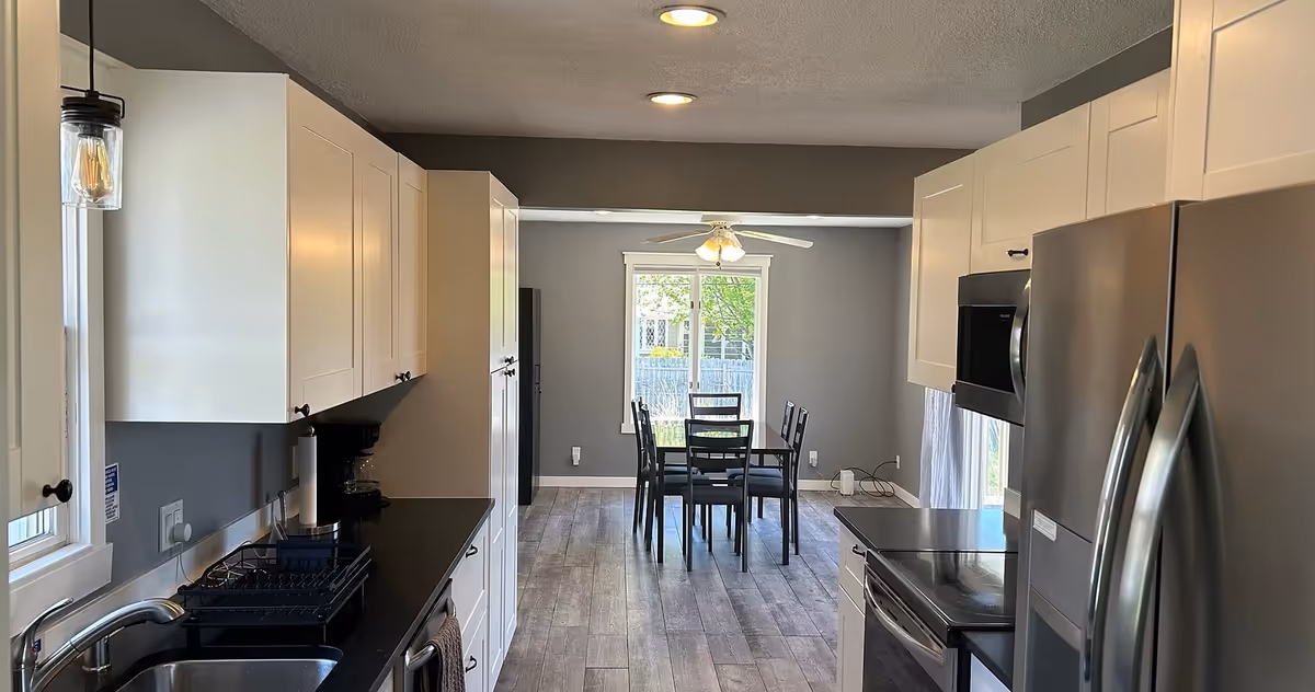 Modern kitchen with white cabinets leads to a dining area with a central table and chairs.