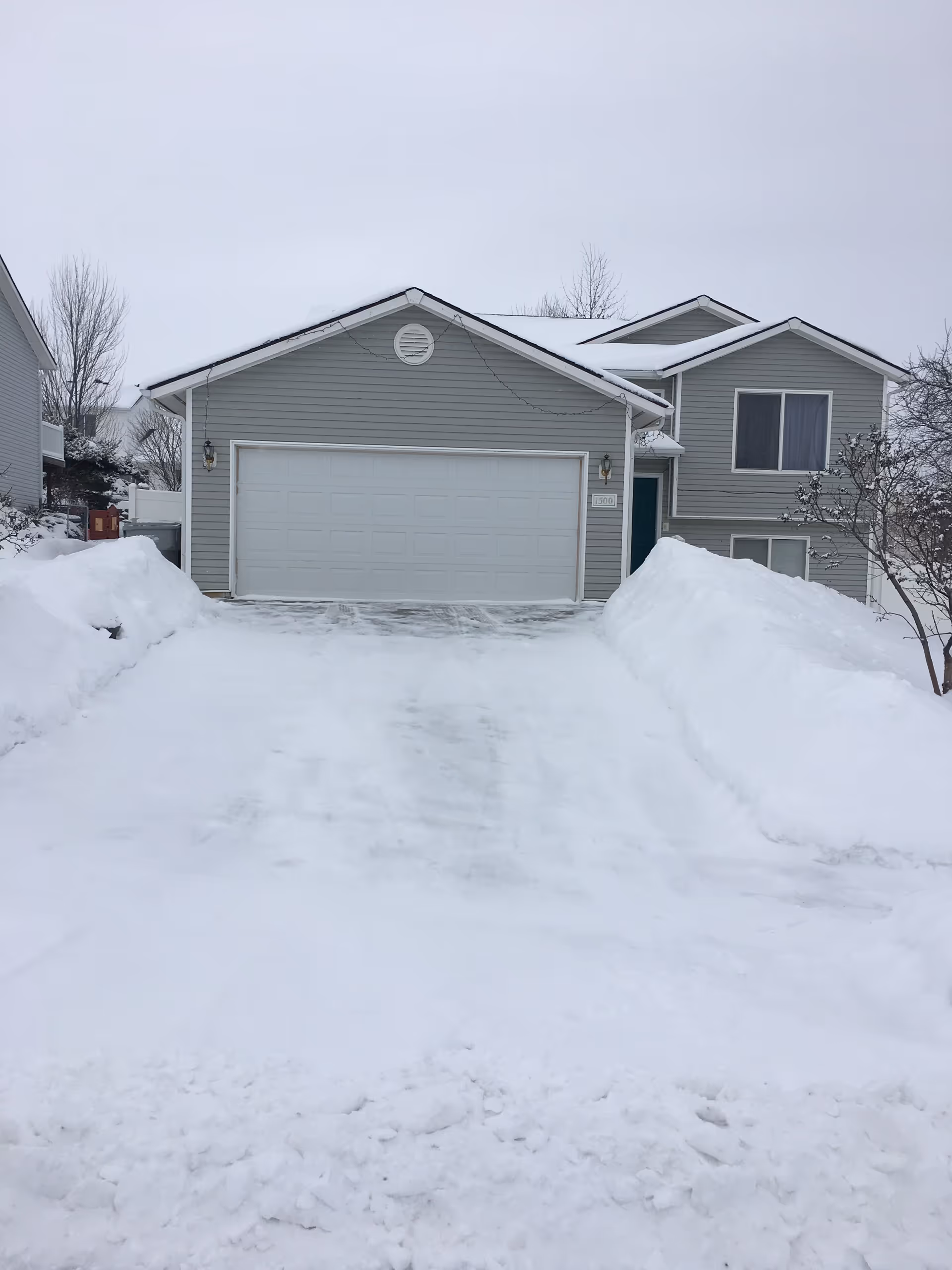 Snow-covered front exterior of a suburban house with a two-car garage.