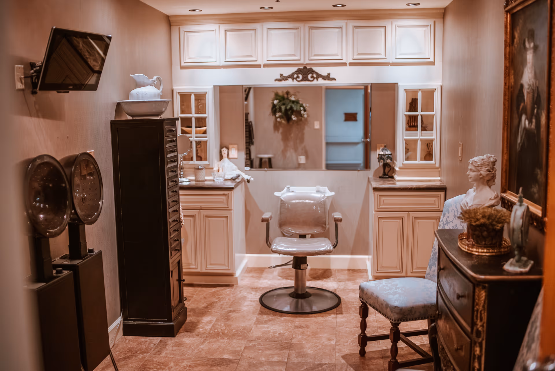 A small salon-style room with a central styling chair facing a framed mirror, cabinetry, and decorative furniture.