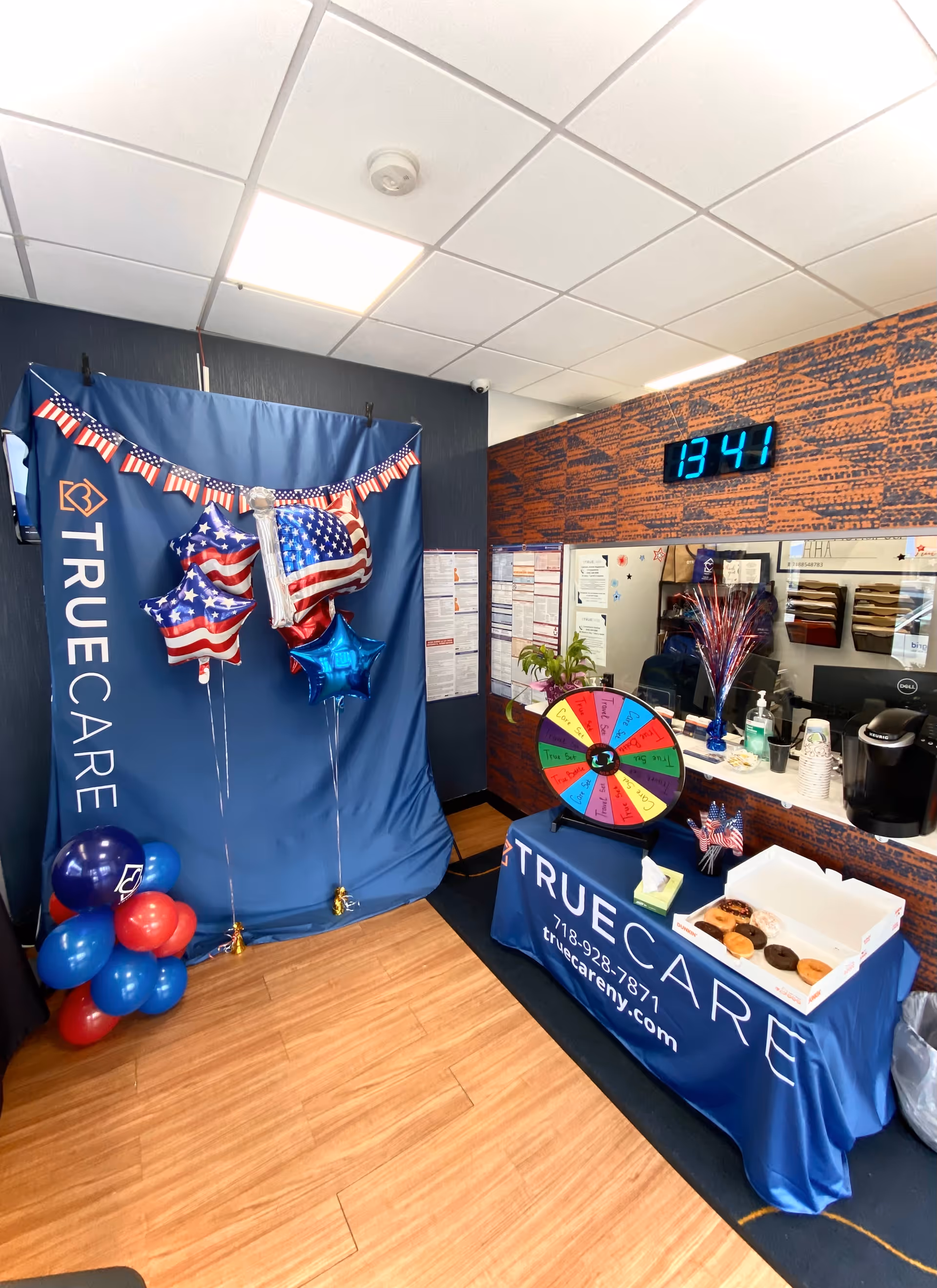 Indoor reception area featuring TrueCare banners, balloons, a spinning wheel, and a service counter.